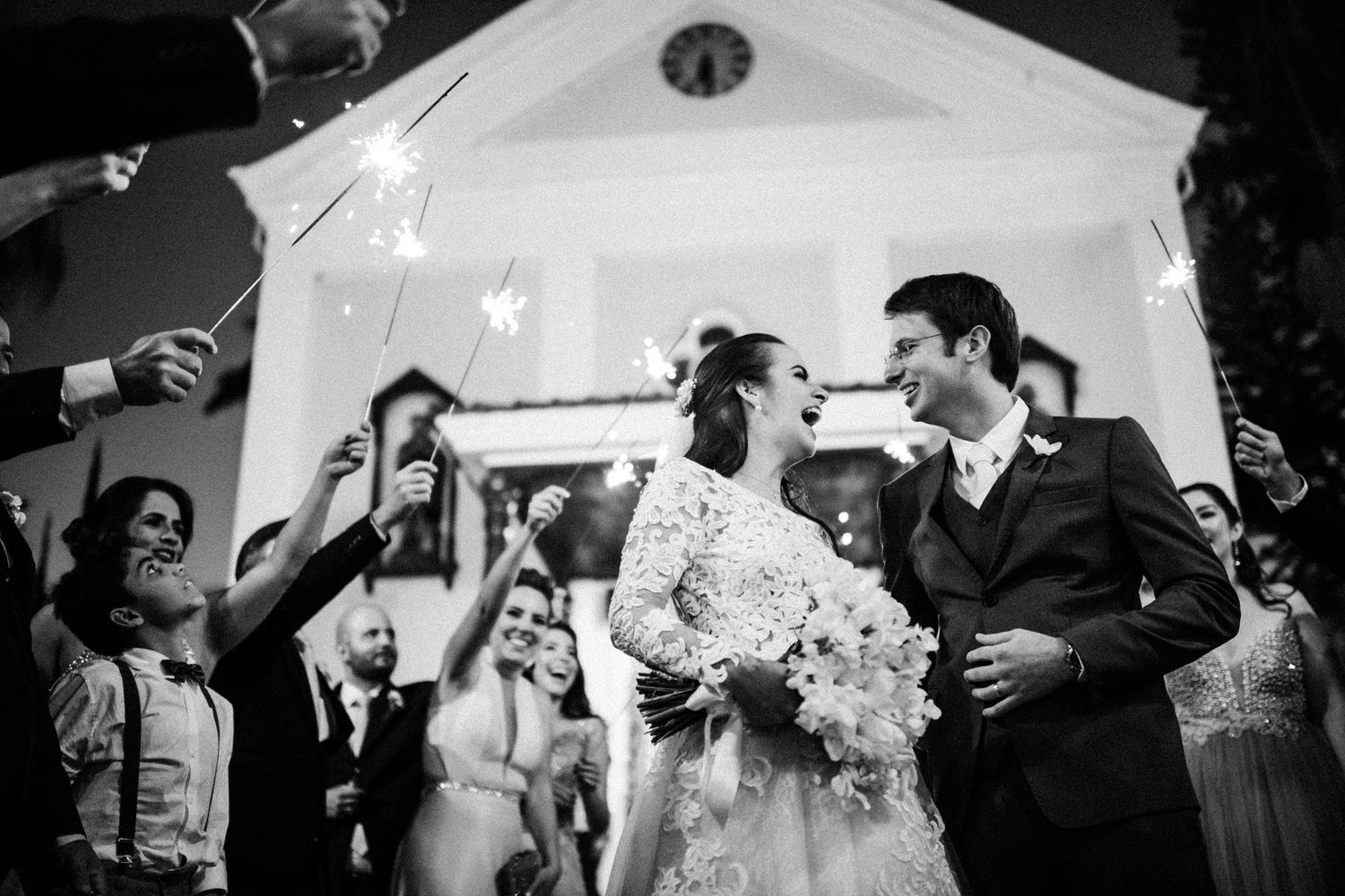 Black and white photo of newlyweds exiting church under sparkler celebration.