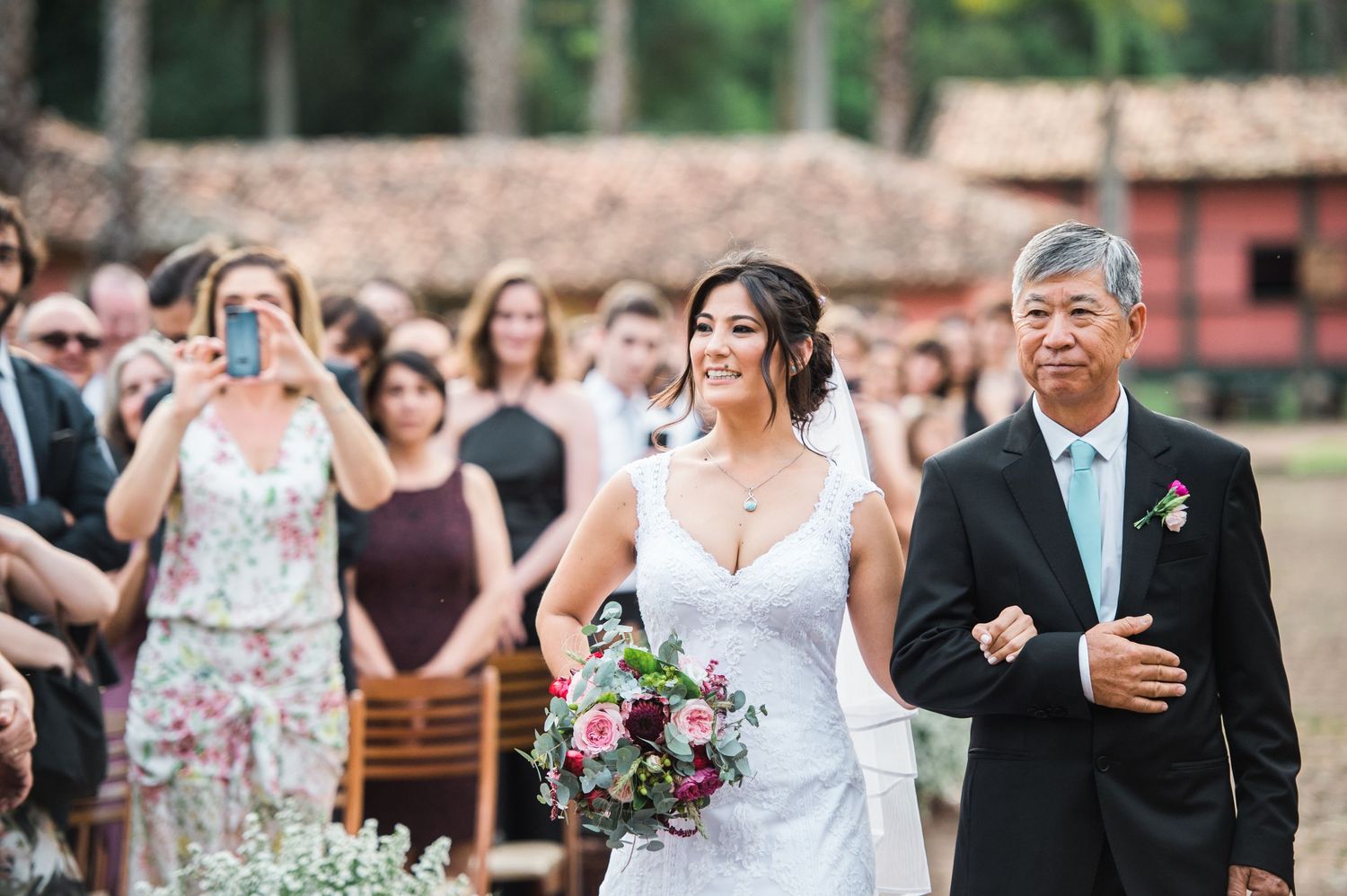 Wedding ceremony with guests seated outdoors near a coral-colored building.