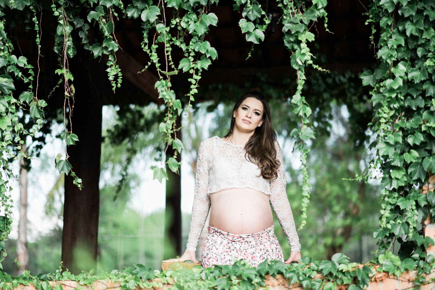 Maternity portrait session in lush garden setting with green foliage backdrop.