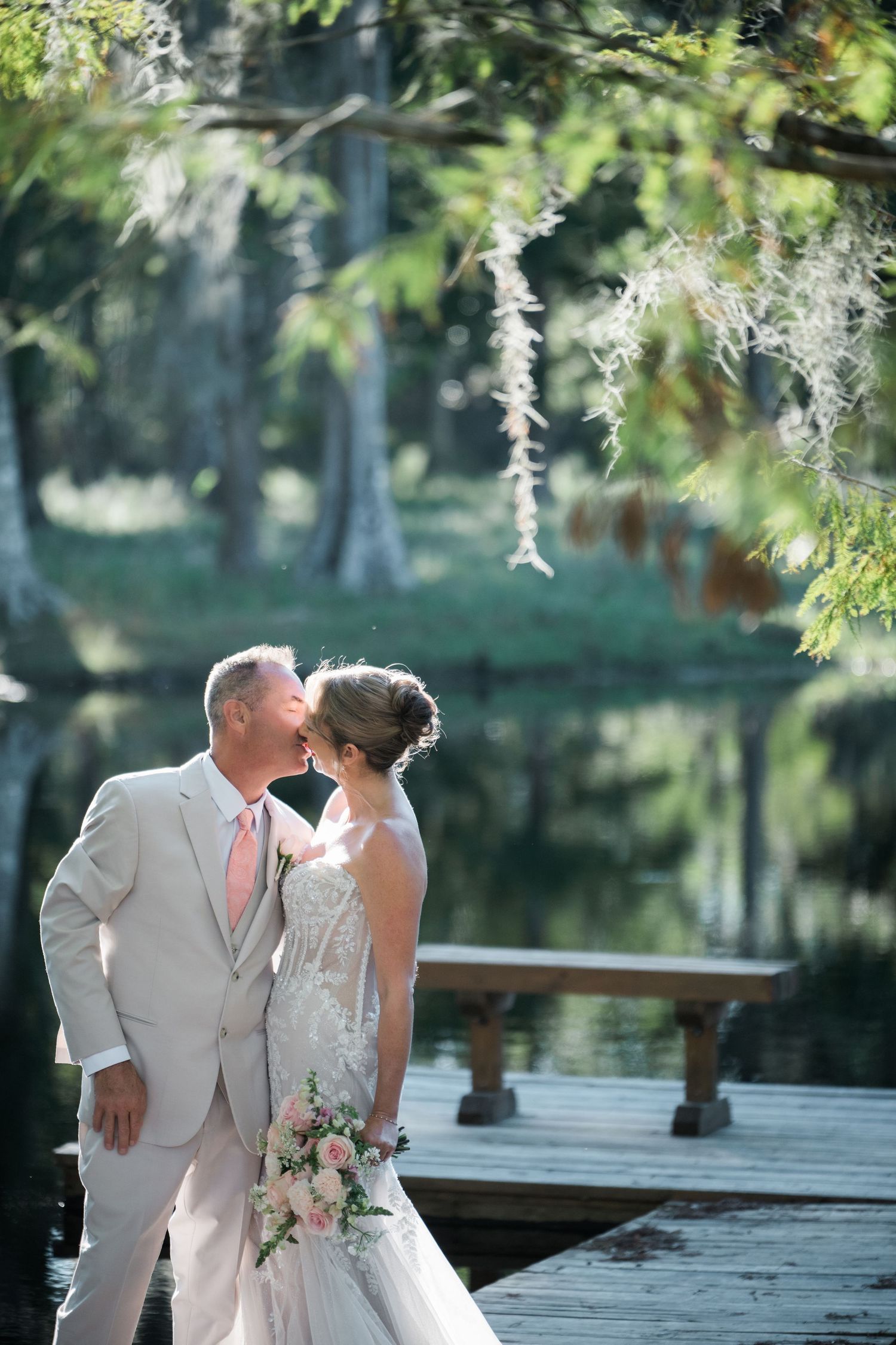 Elegant couple sharing a moment on a wooden dock surrounded by trees.