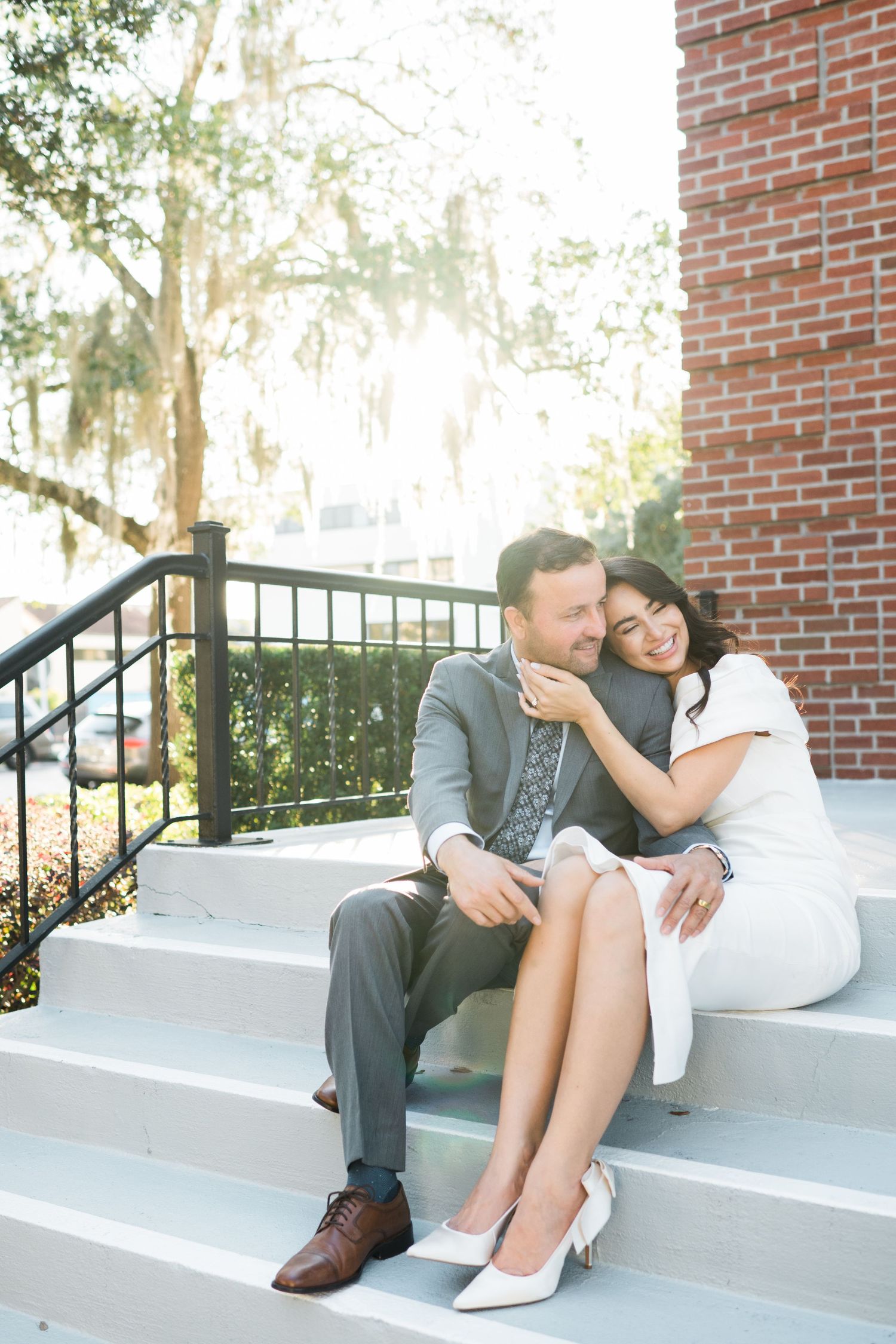 A couple shares an intimate moment sitting on concrete steps against a brick wall backdrop.