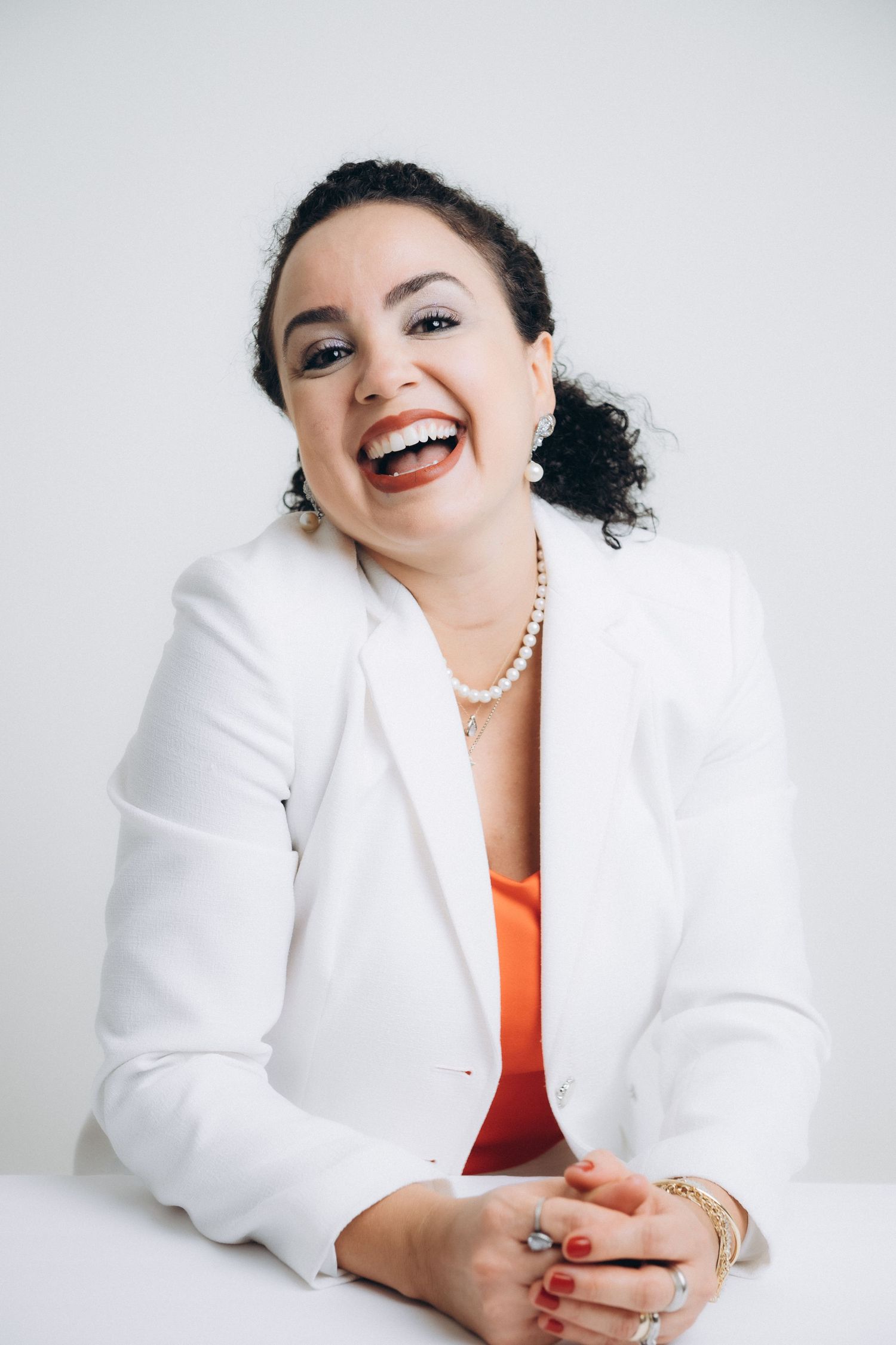 Professional portraits in white blazer and orange top against light background.
