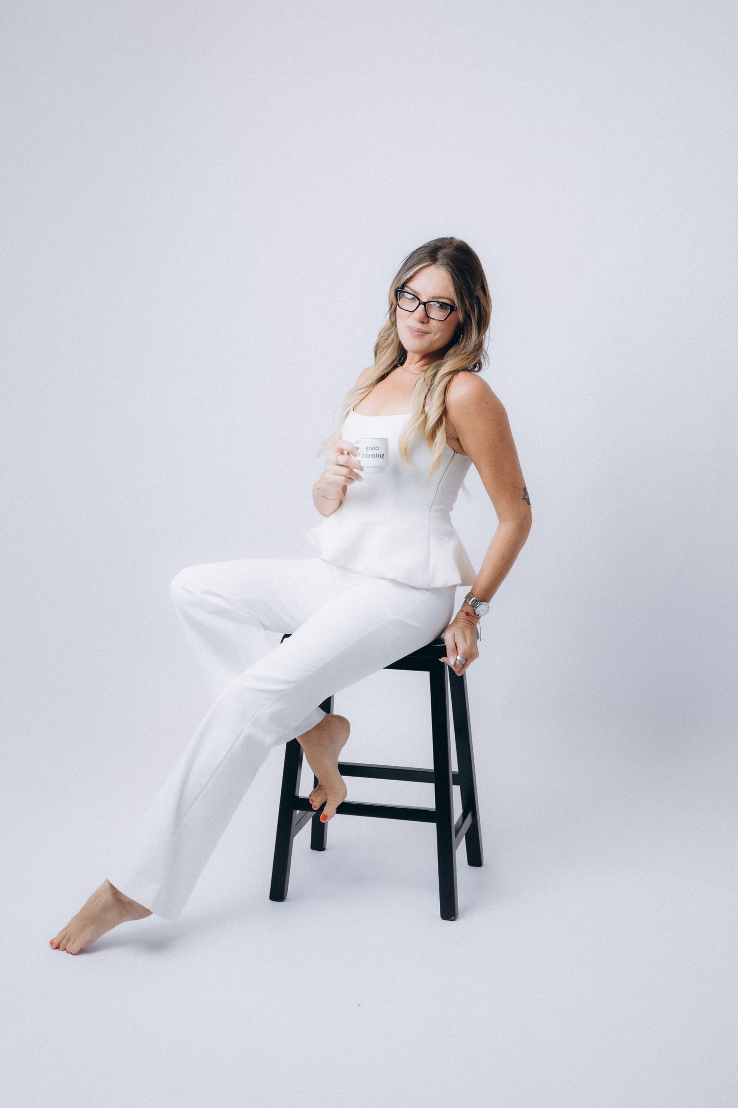 Studio portrait session featuring white outfit and relaxed poses on black stool.