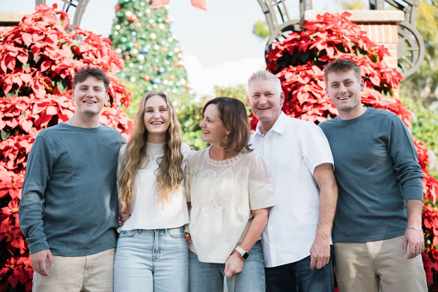 Family group in coordinated casual outfits poses against red floral backdrop.