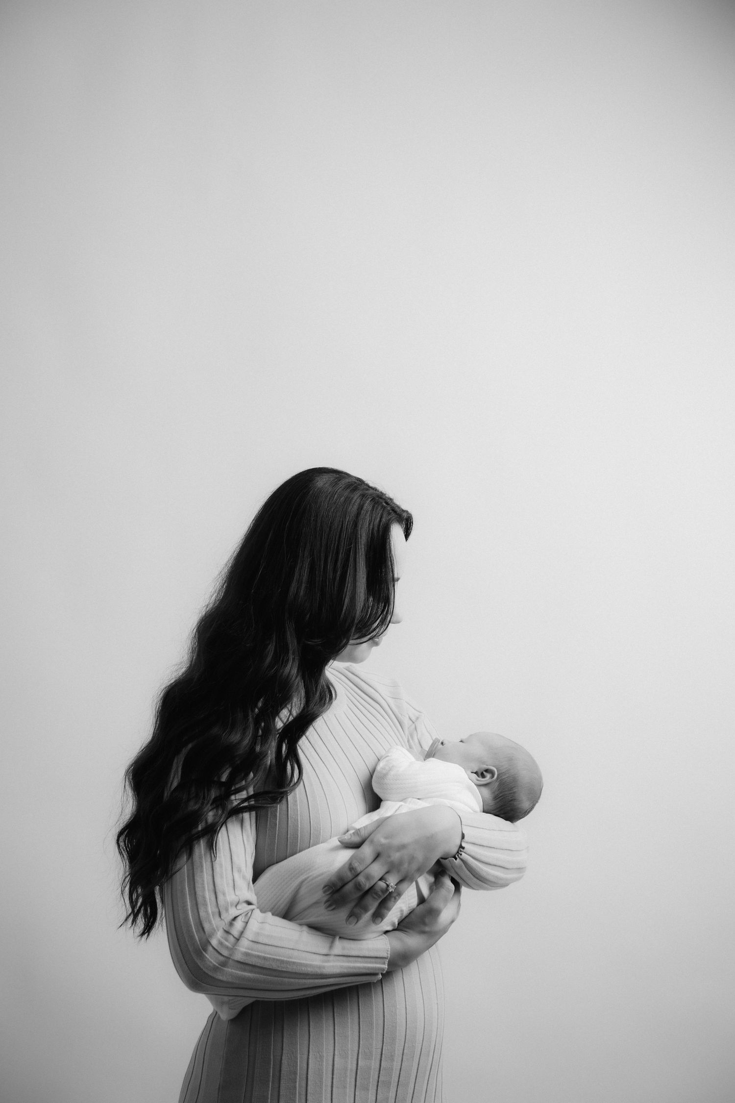 Black and white portrait of person with long hair holding infant in tender embrace.