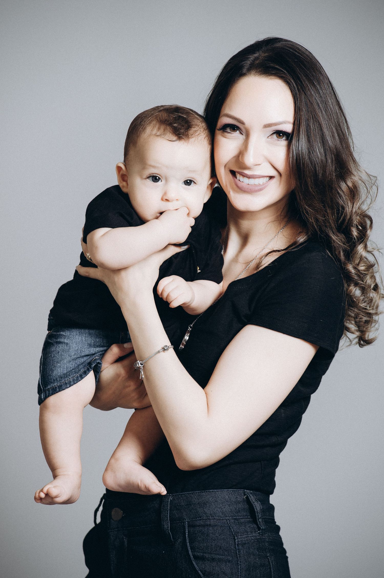 Mother and baby in black outfits pose playfully against a light gray backdrop.