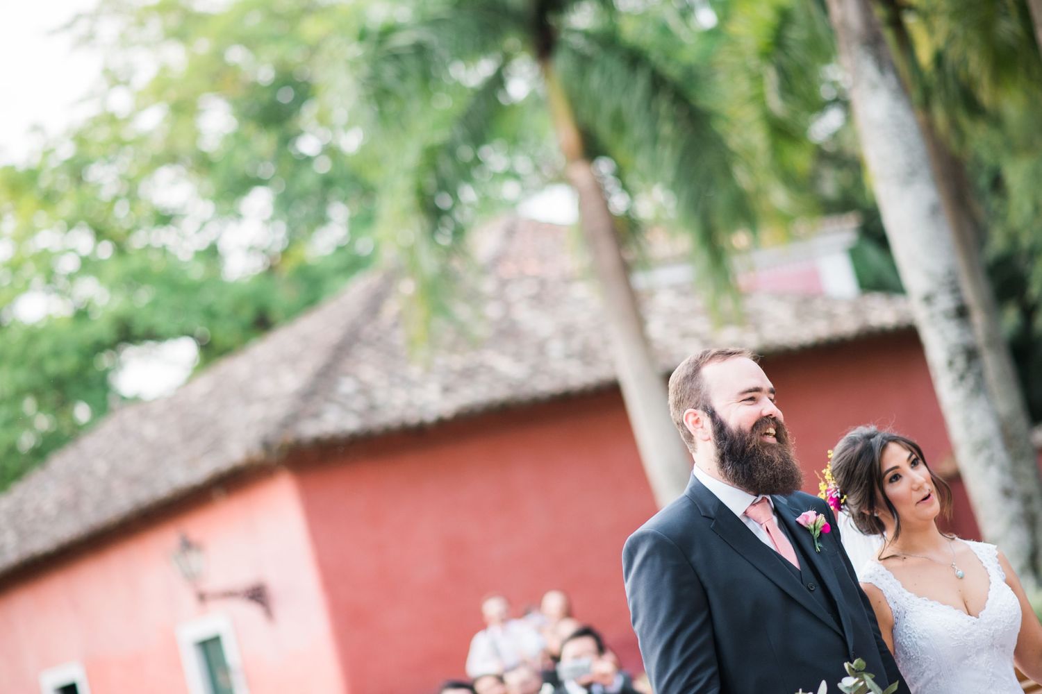 Outdoor wedding celebration with lush greenery and a coral building backdrop.