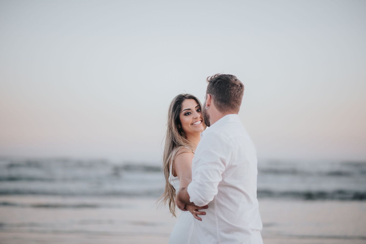 Romantic couple embracing on a beach during golden hour.
