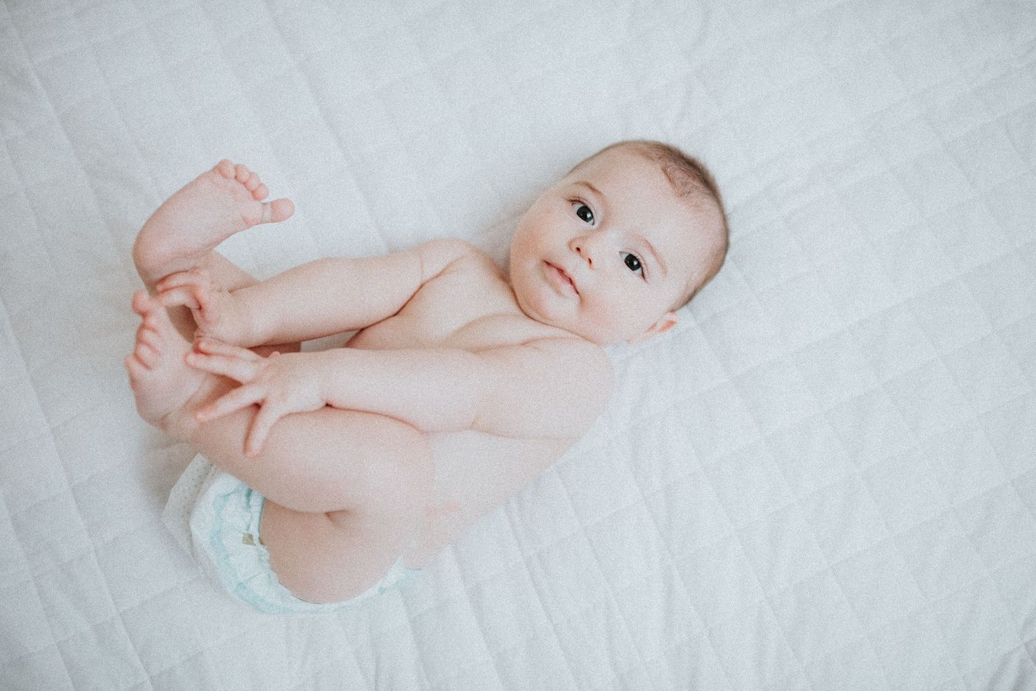 Baby lies on white blanket during natural light portrait session.