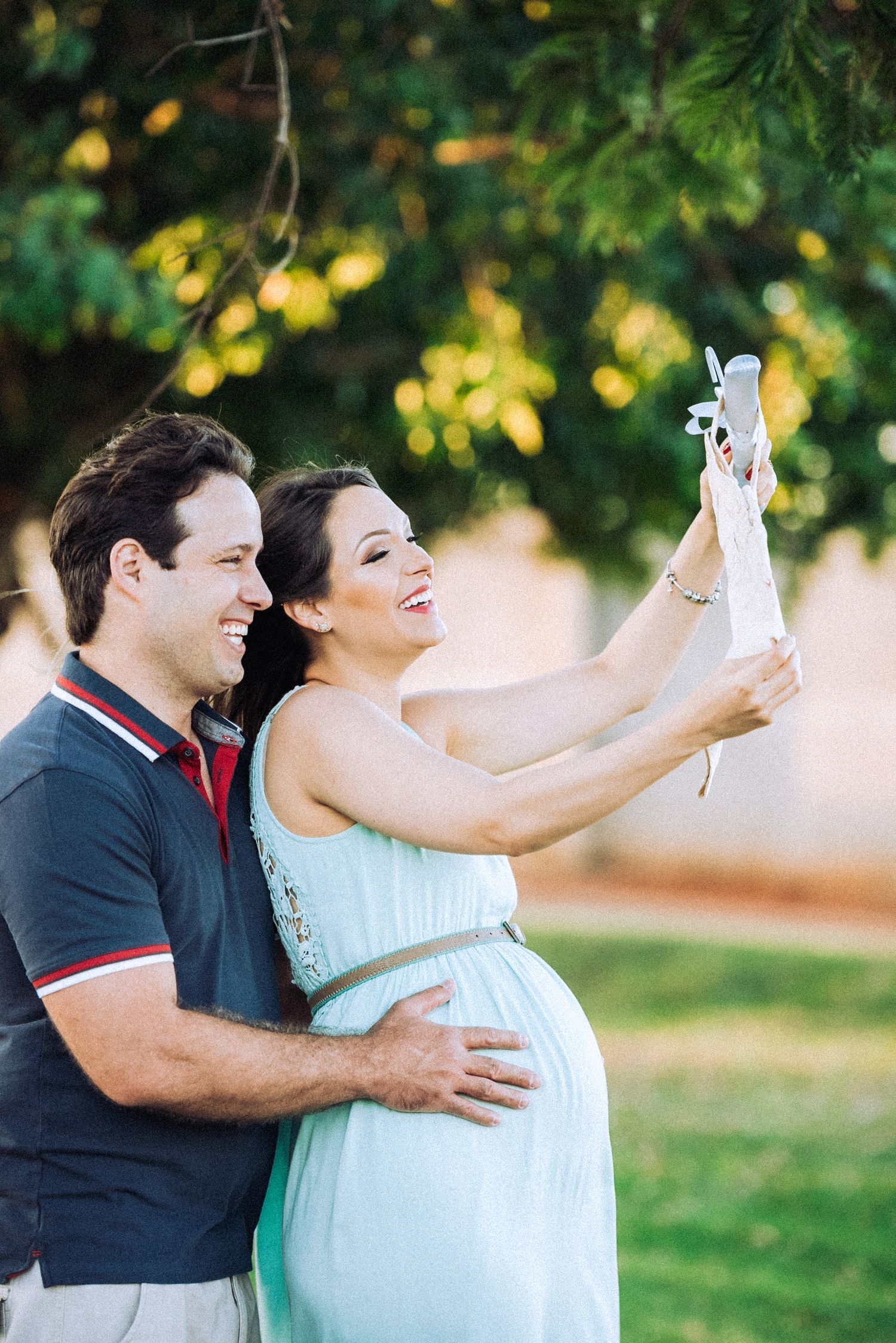 Expectant couple holding baby shoes during outdoor photography session.