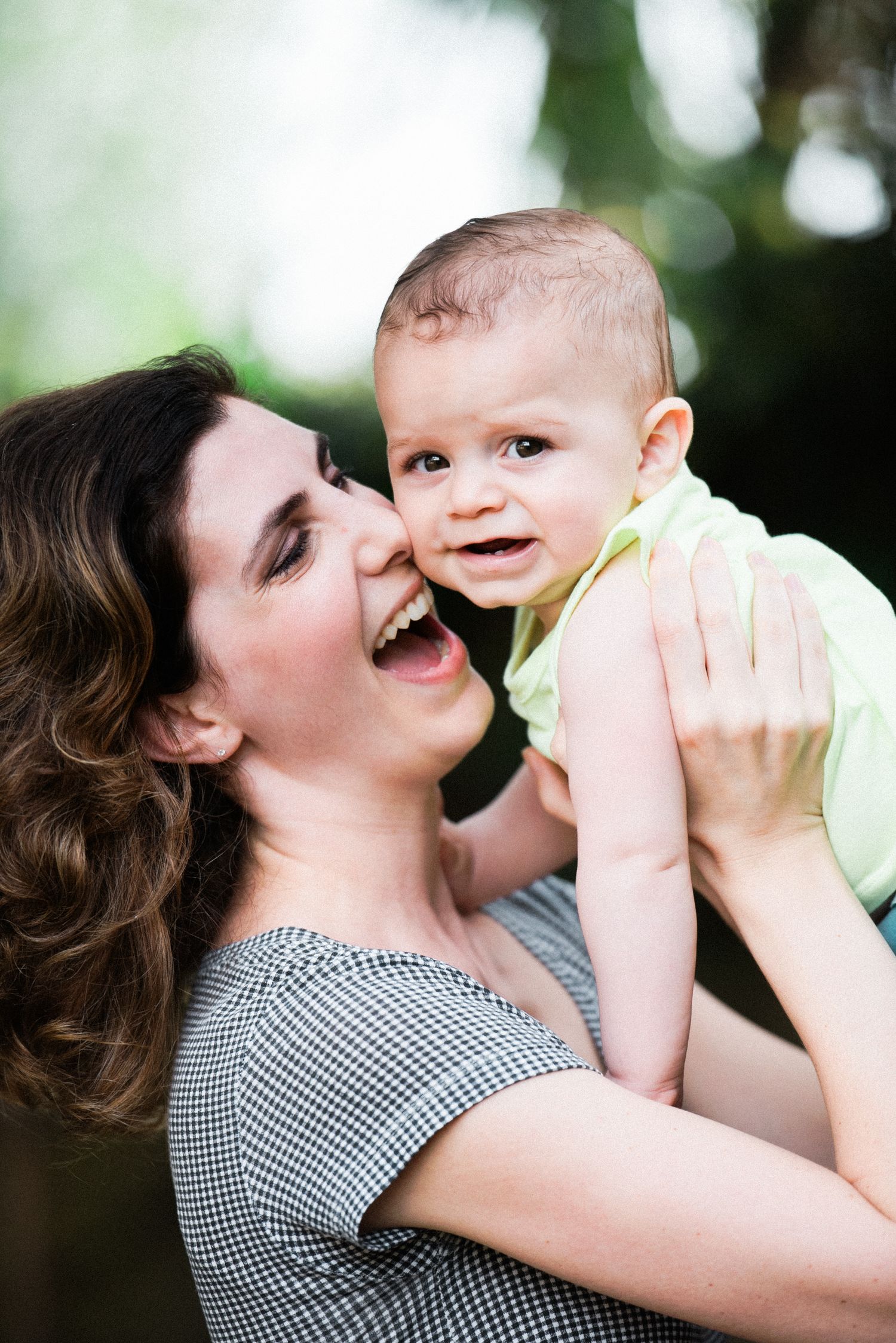 Playful interaction between adult and baby outdoors with natural bokeh background.