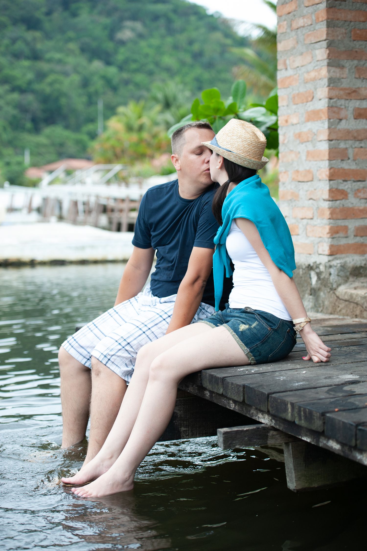 Two people sitting on a wooden dock with their feet dangling over the water.