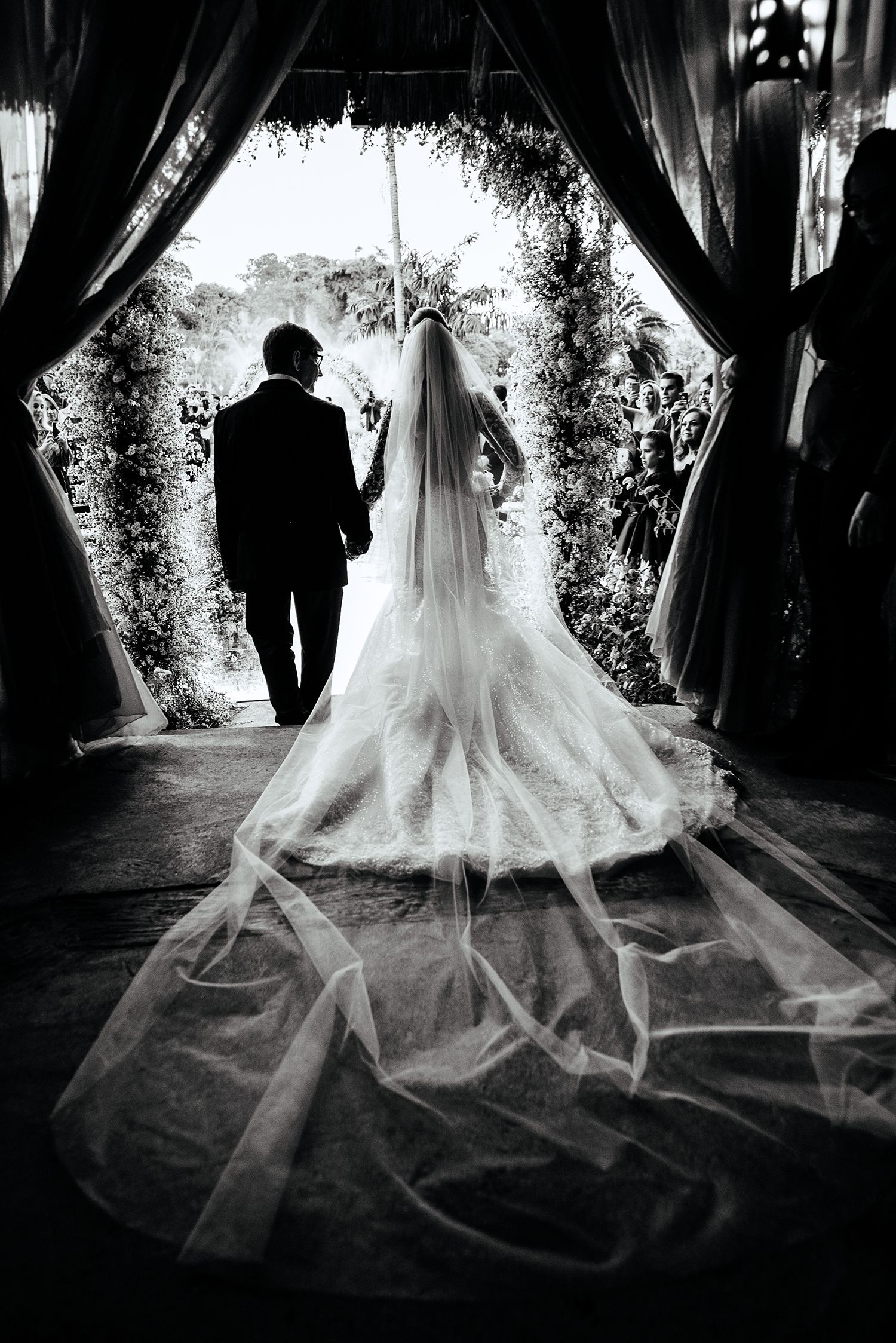 Silhouette of a bride and groom under an archway with flowing veil in black and white photography.