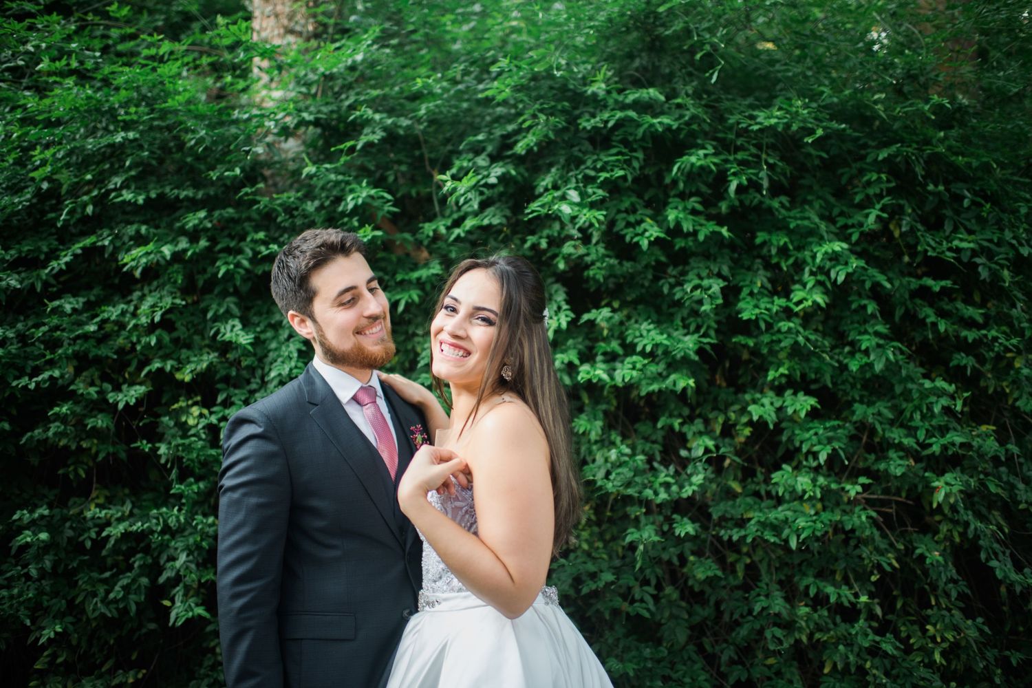 Wedding couple shares romantic moments against a backdrop of green foliage.