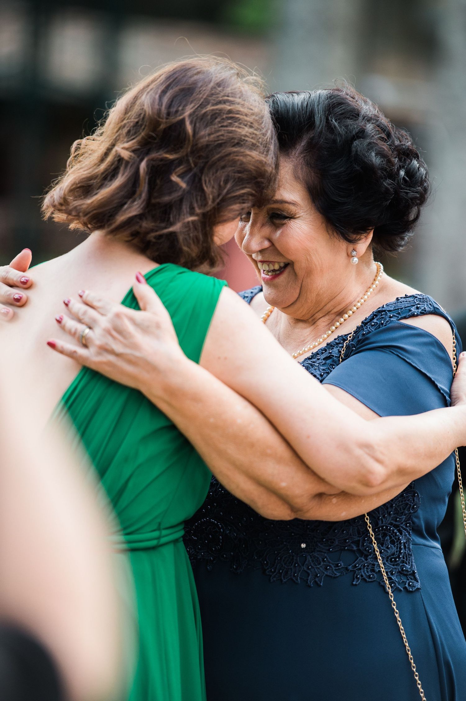 Close-up of emotional embraces between guests wearing green and navy at a wedding.