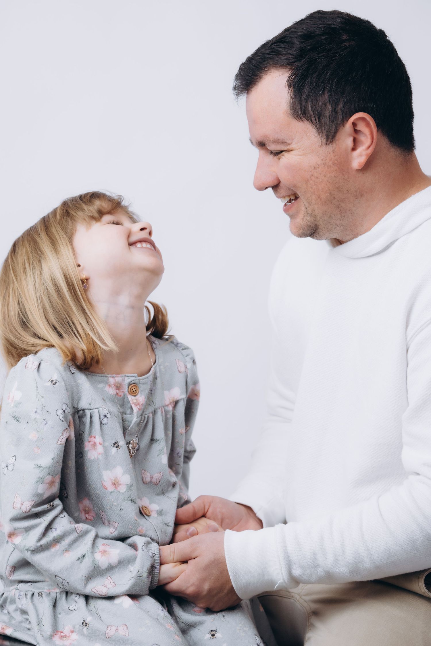 Parent and young child share a joyful laughing moment together against white background.