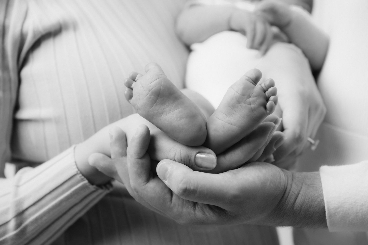 Black and white image of tiny baby feet being held in adult hands.