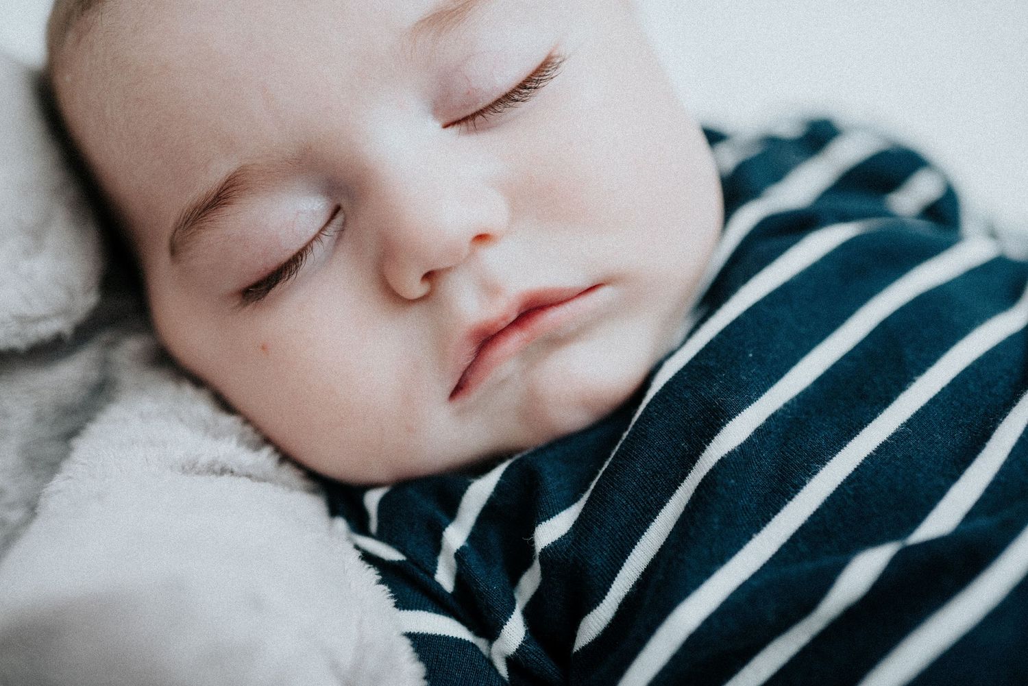 Sleeping baby in striped outfit rests peacefully on white bedding.