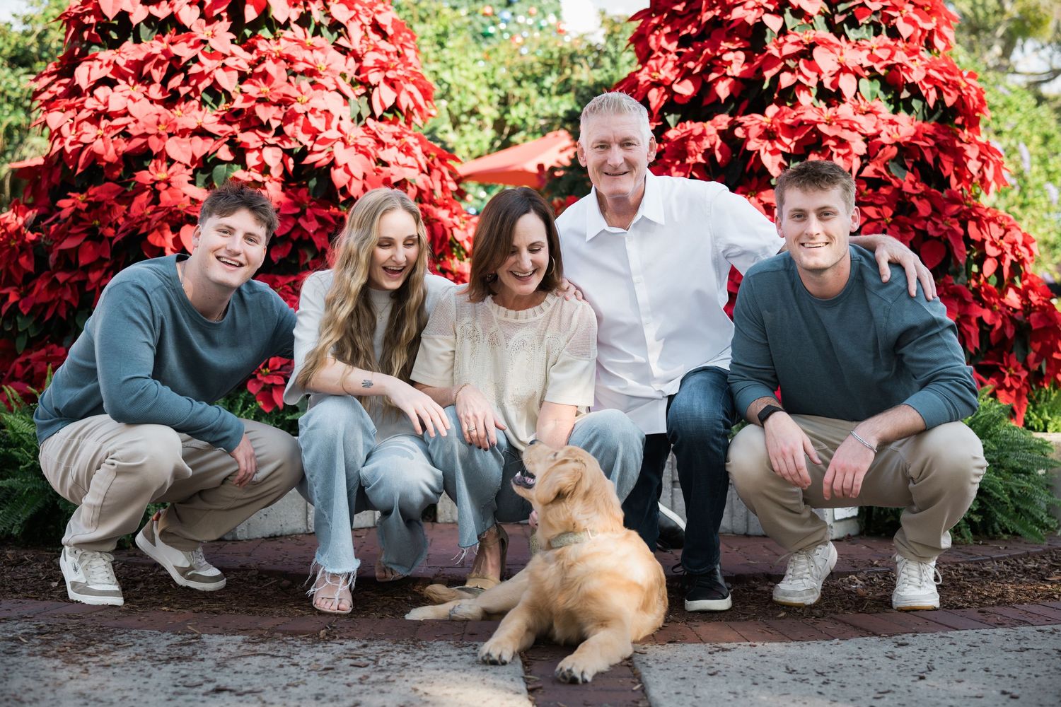 Casual family portrait with pet dog against vibrant red poinsettia background.