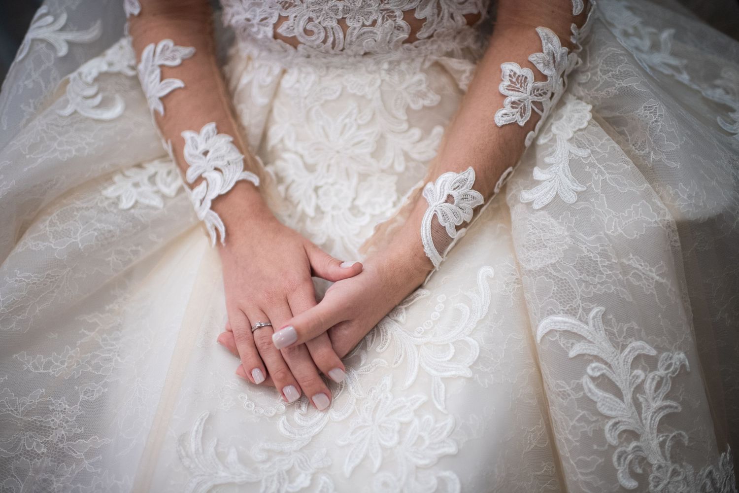 Detail shot of hands resting on layers of white tulle and lace wedding dress fabric.