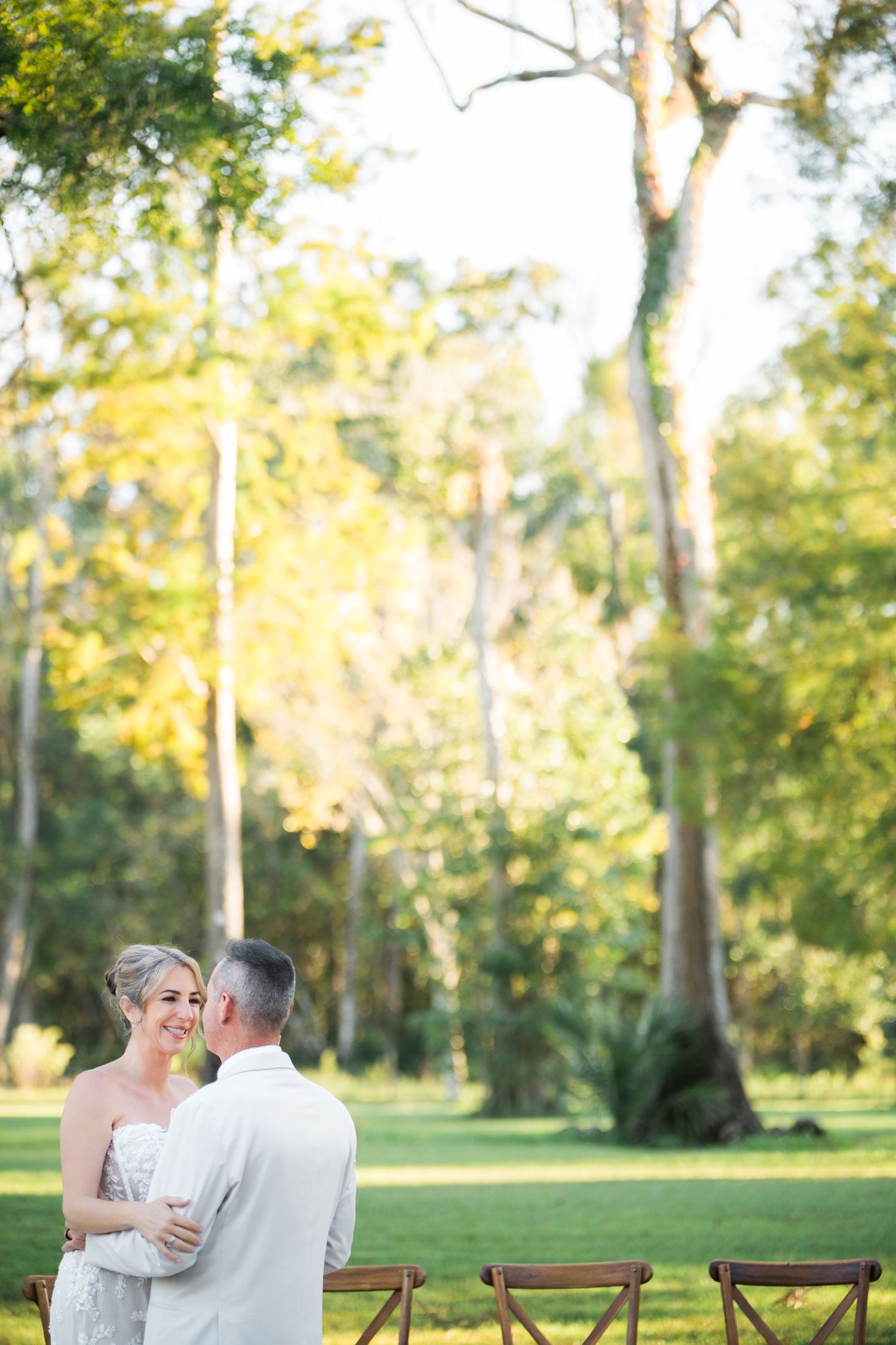 A couple dances together outdoors with wooden chairs and lush greenery in the background.