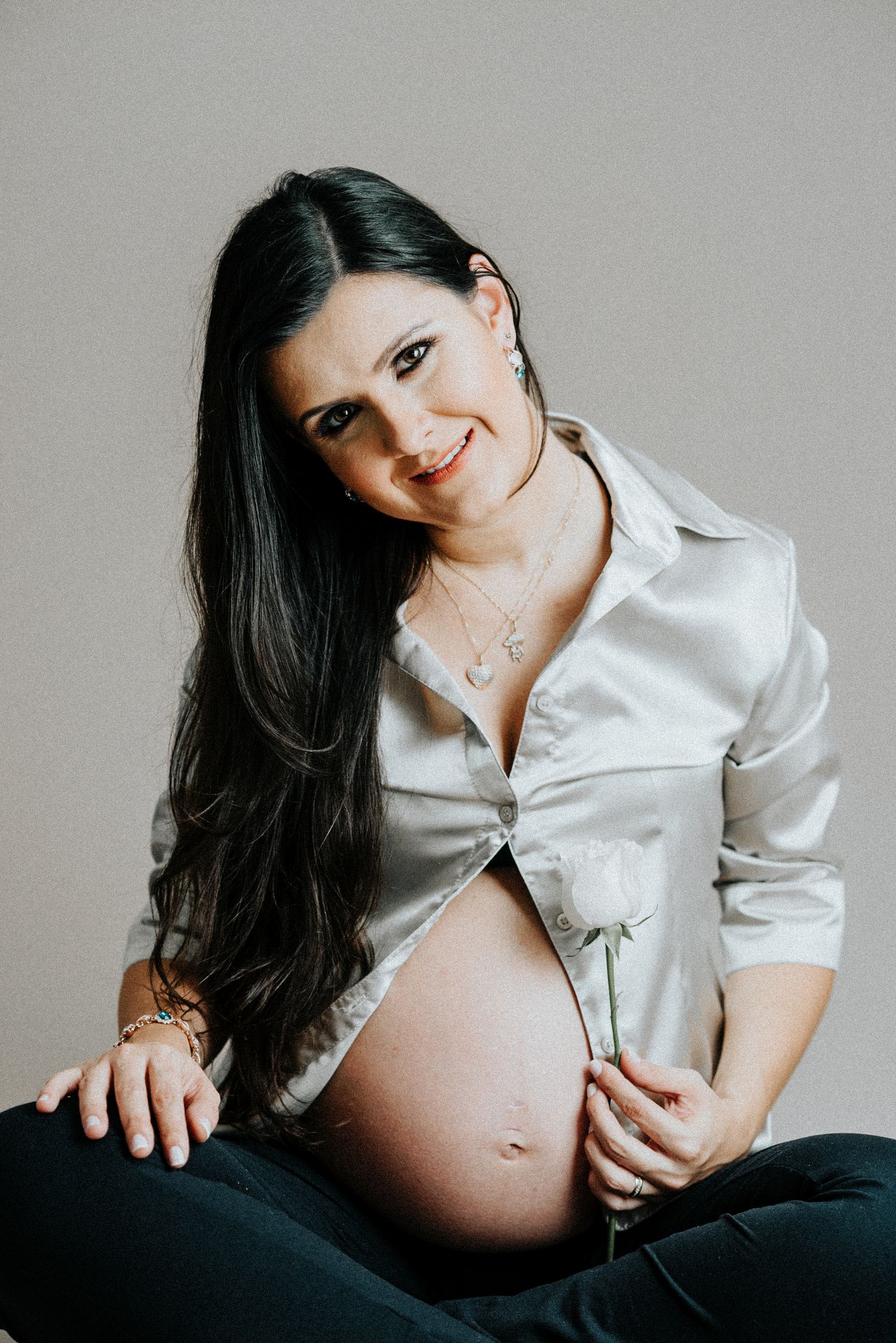 Maternity photo of woman in white button-down shirt against grey backdrop.