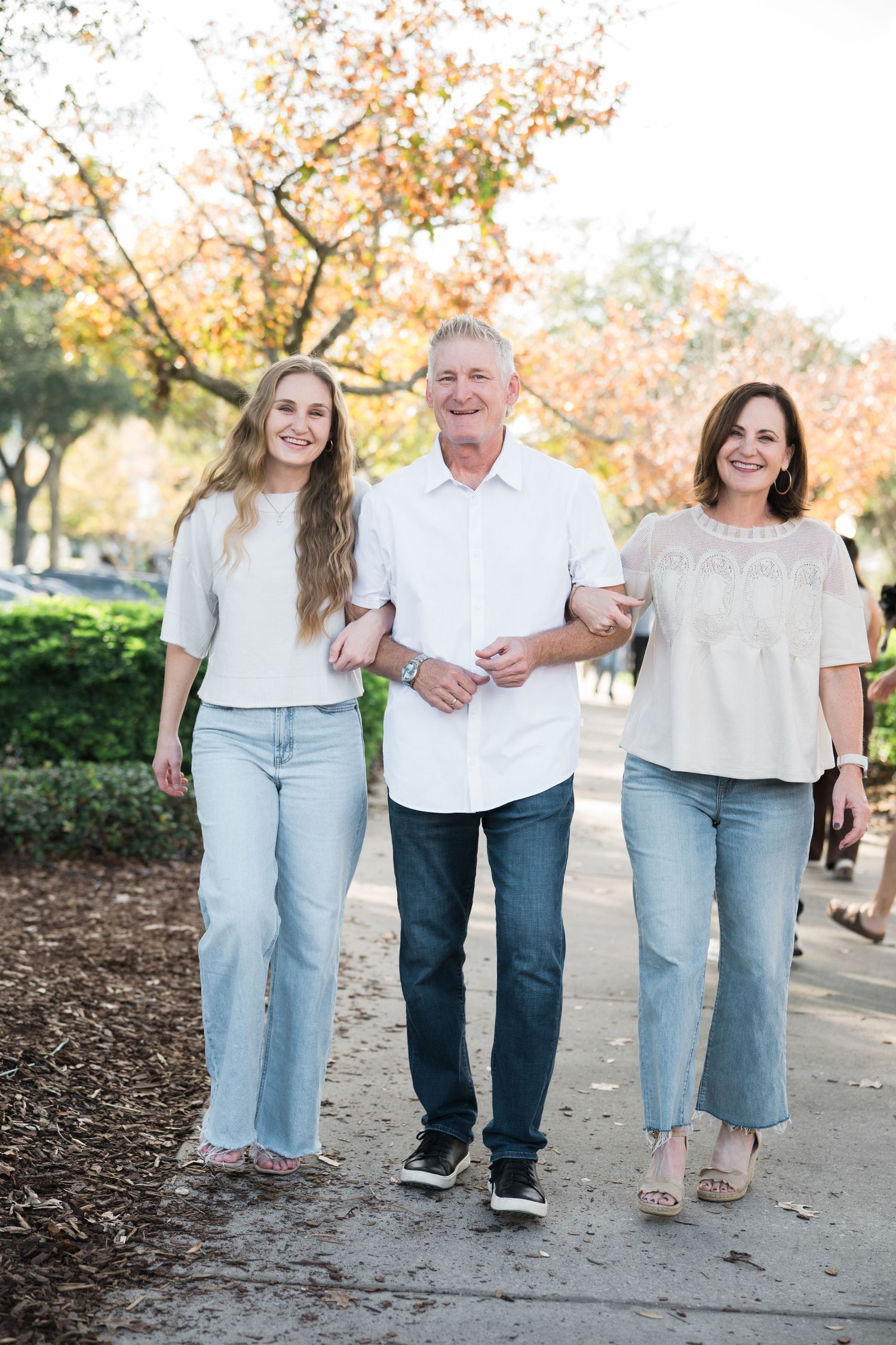 Casual family photo session showing coordinated outfits in white tops and jeans walking together on a fall day.