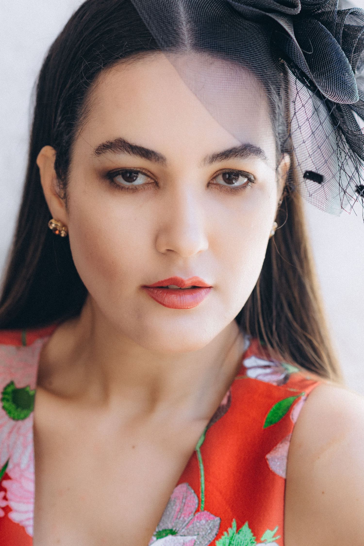 A red floral dress accessorized with a black fascinator hat in a portrait series.