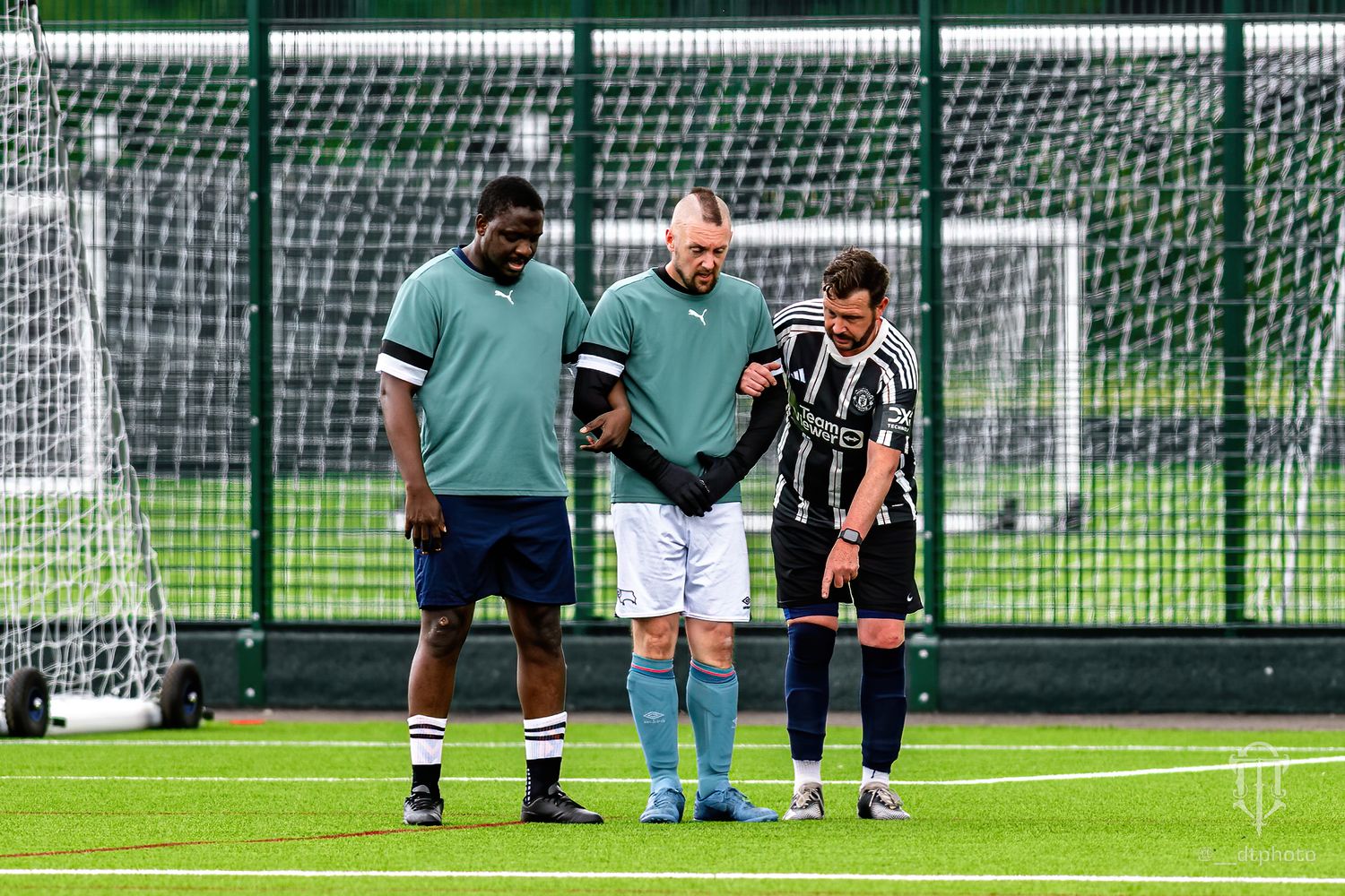 Players in green and black uniforms gather near the goal during a football match.