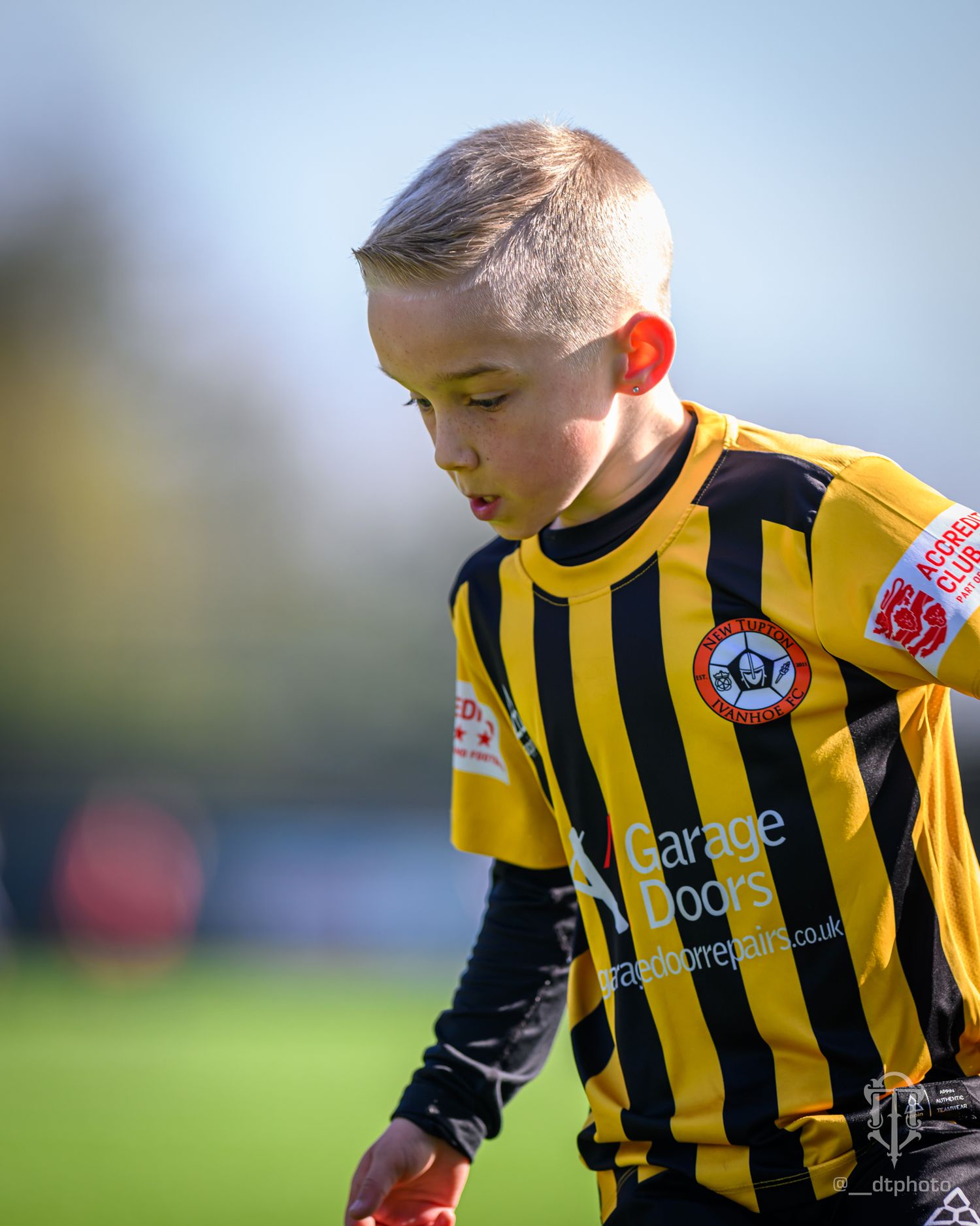 Young soccer player in yellow and black striped jersey focused during a match with team patch visible on uniform.