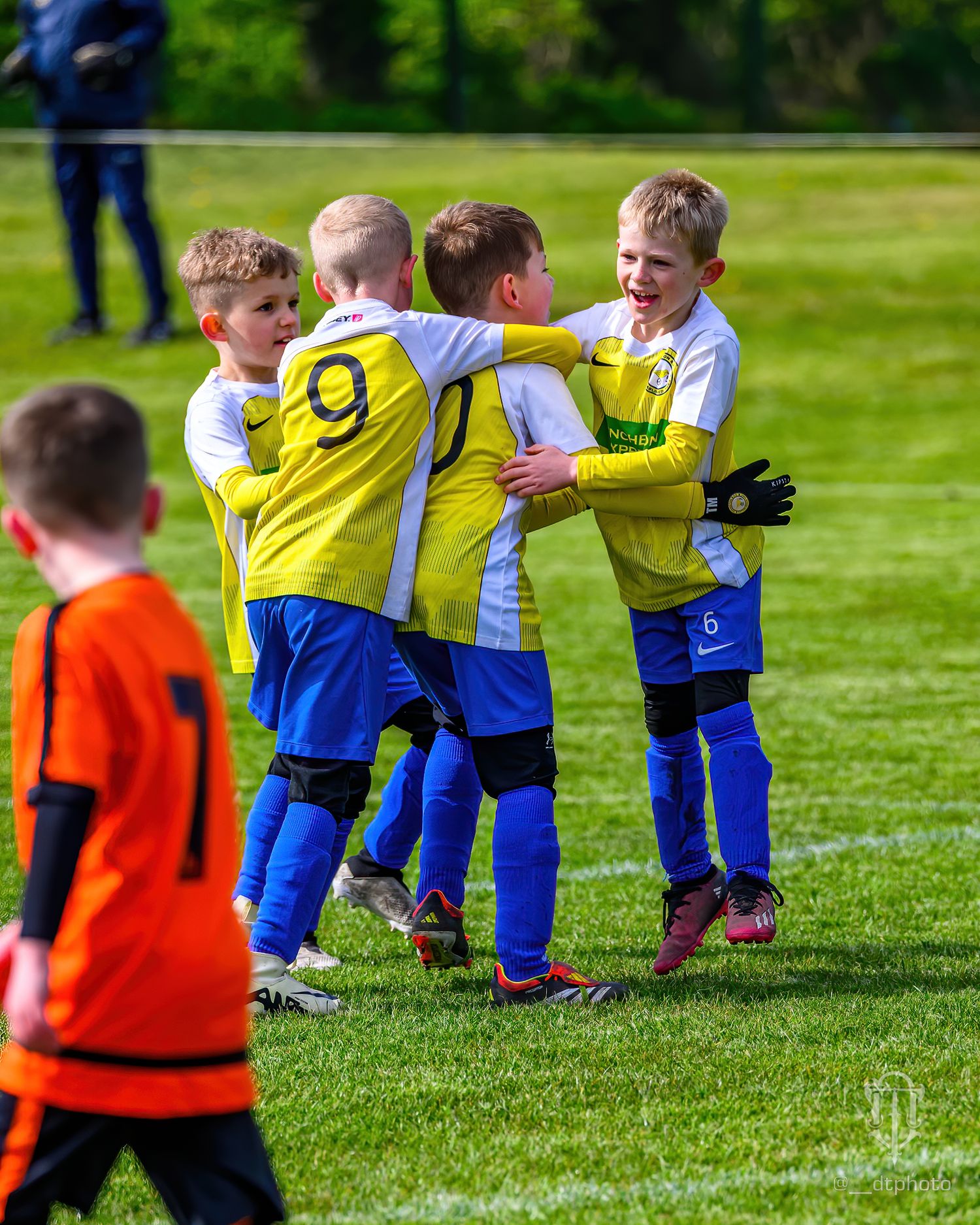 Youth football players in yellow jerseys celebrate together during a match.