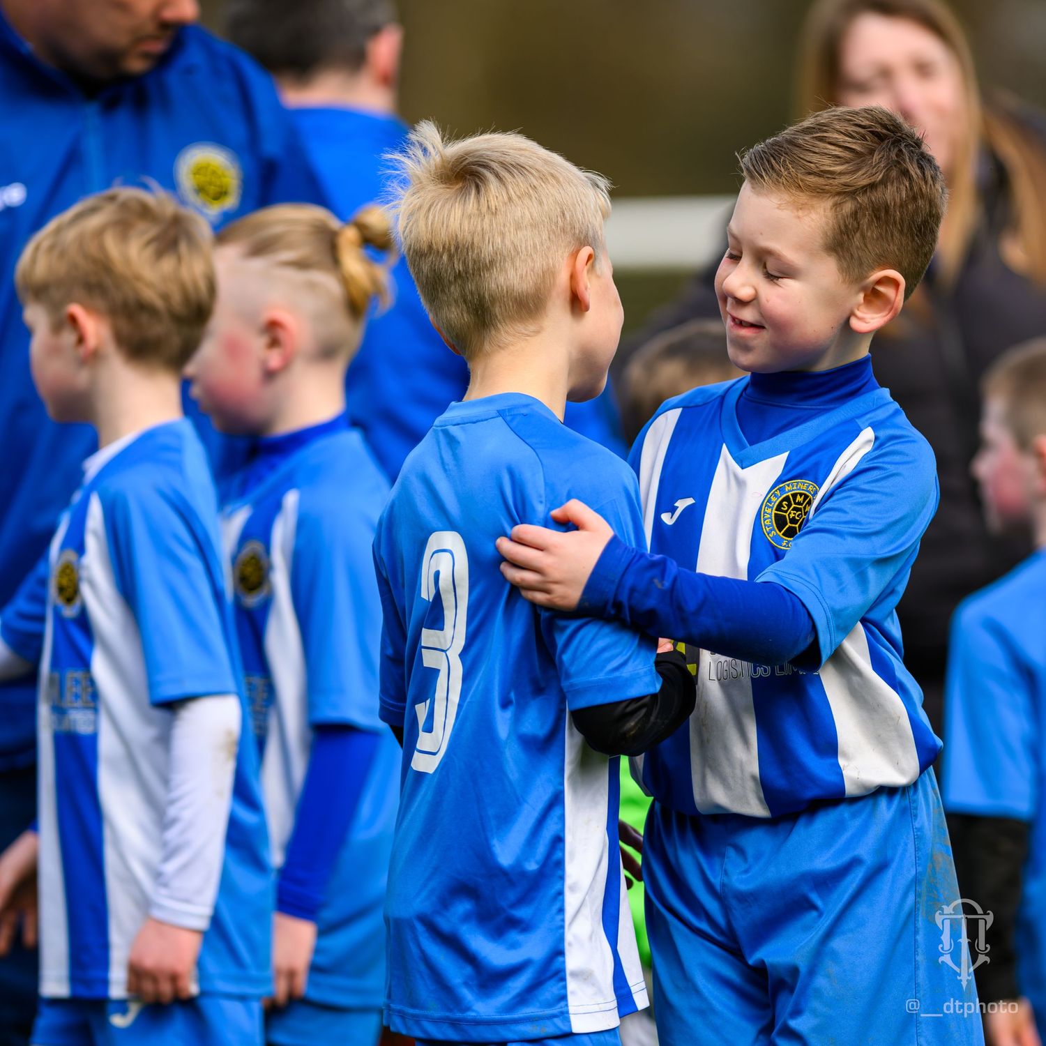 Youth football teammates in blue jerseys share a friendly moment before the game.