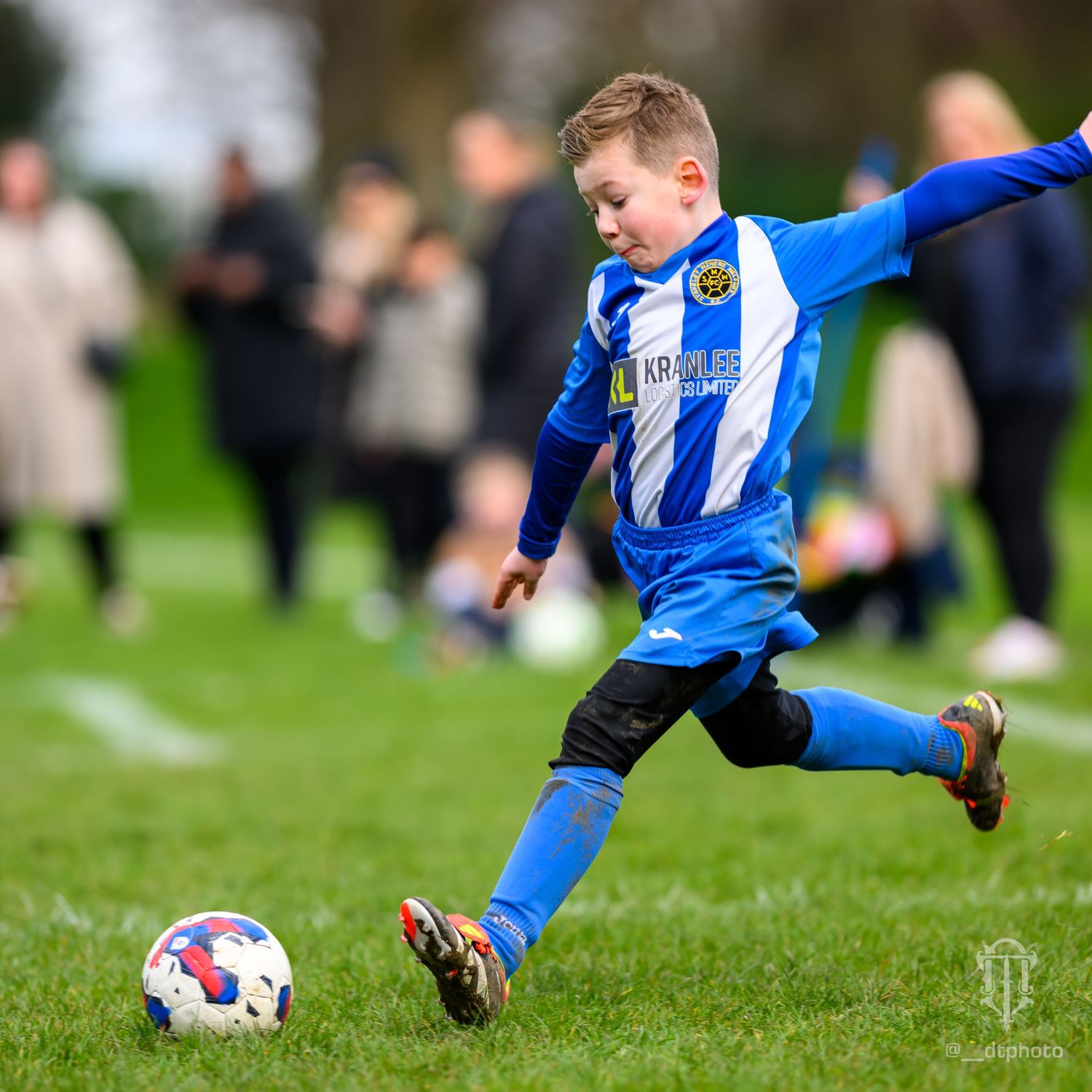 Young player in blue and white uniform kicks soccer ball on grass field.