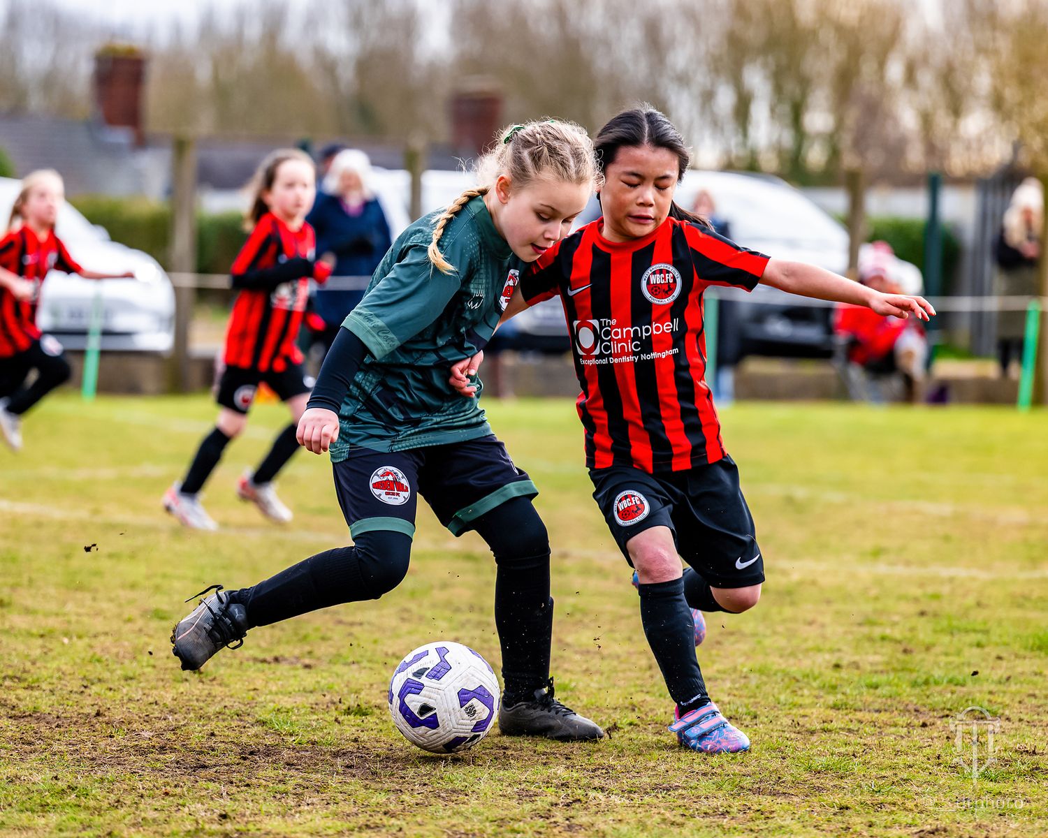 Two youth football players from opposing teams compete for possession of the ball.