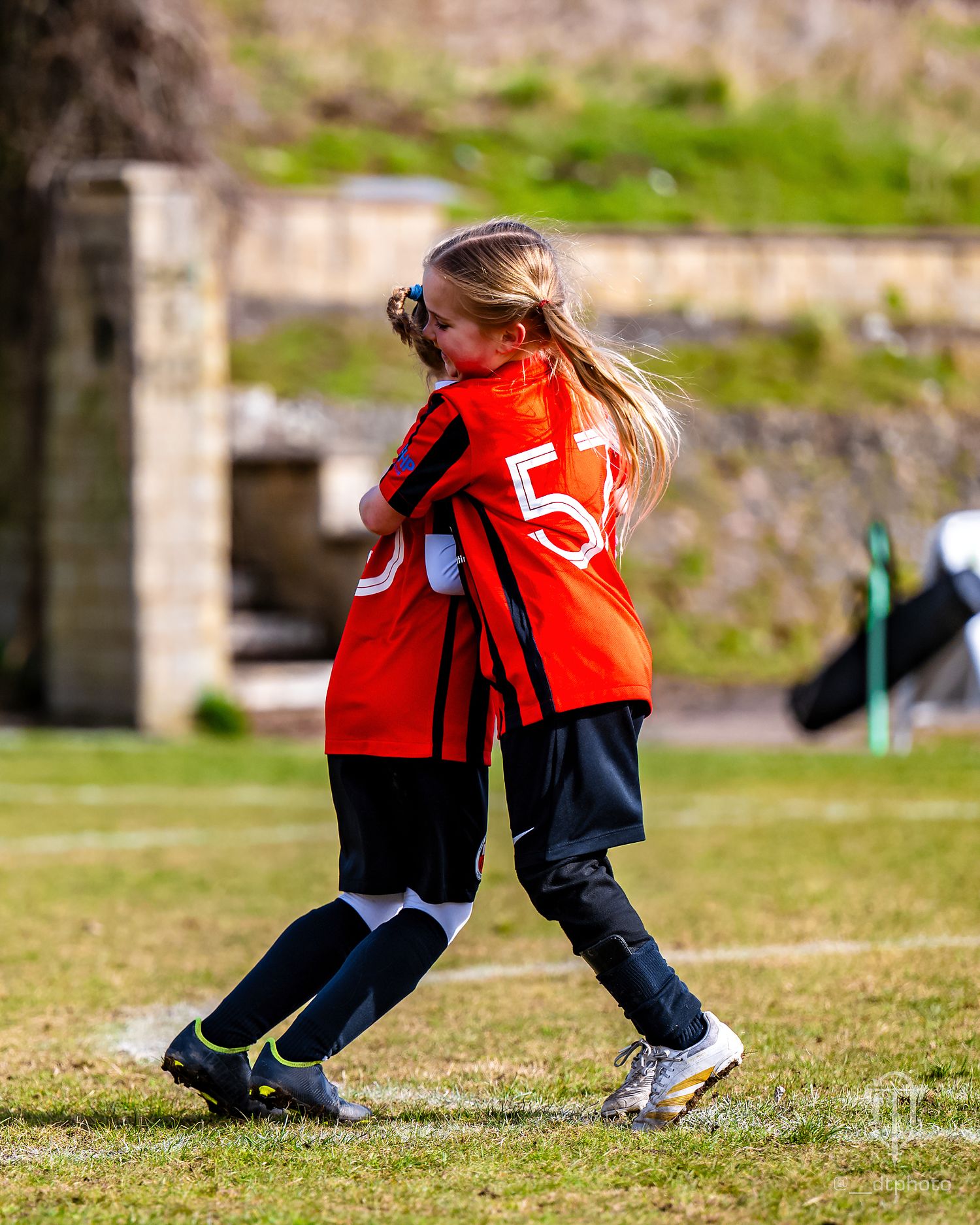 Young football player in red uniform jumps while playing on grass field.