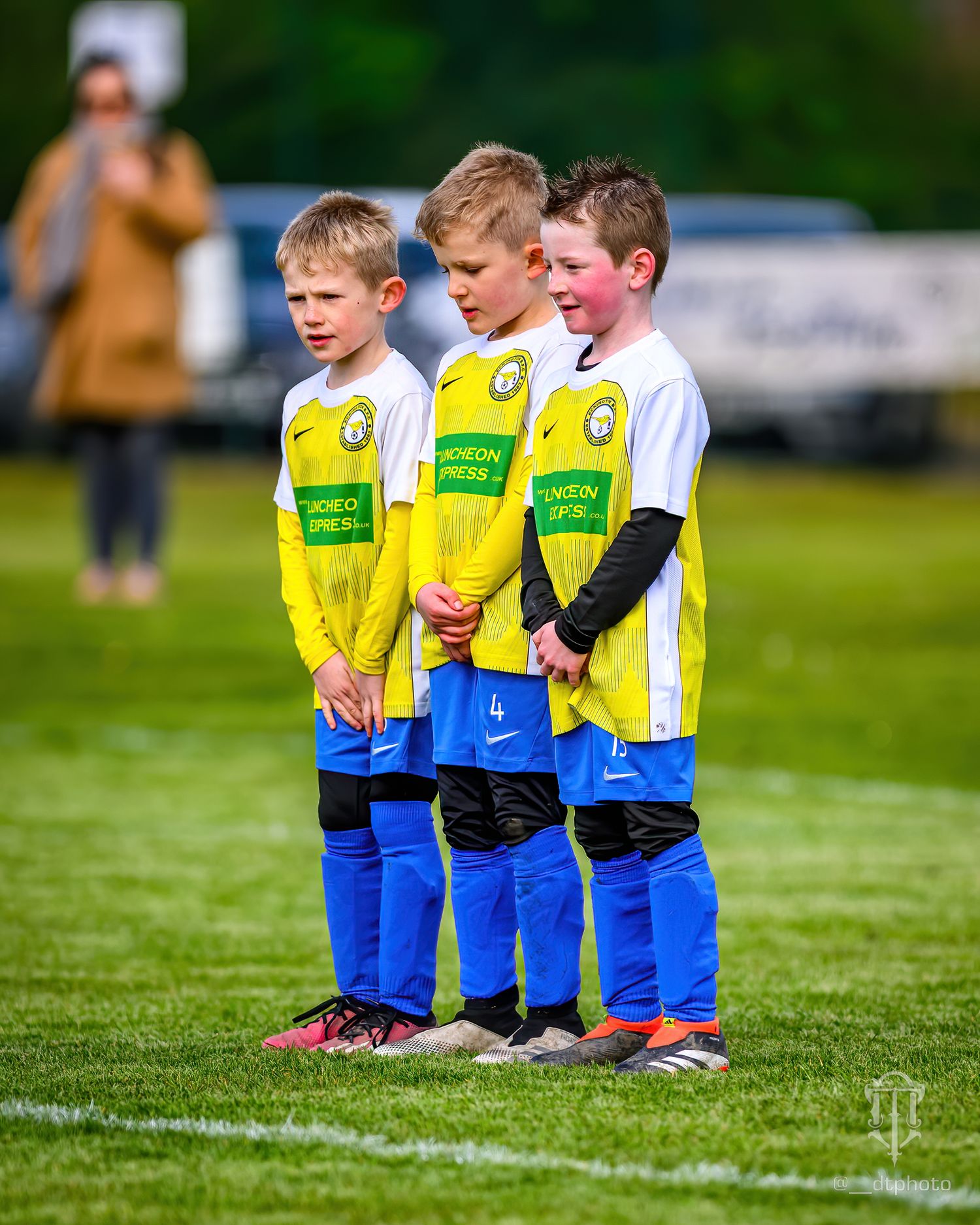 Three young football players in yellow and blue uniforms stand in formation on the field.