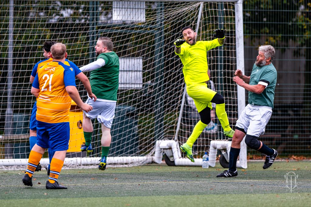 Goalkeeper in yellow makes a dramatic save during an adult football match.