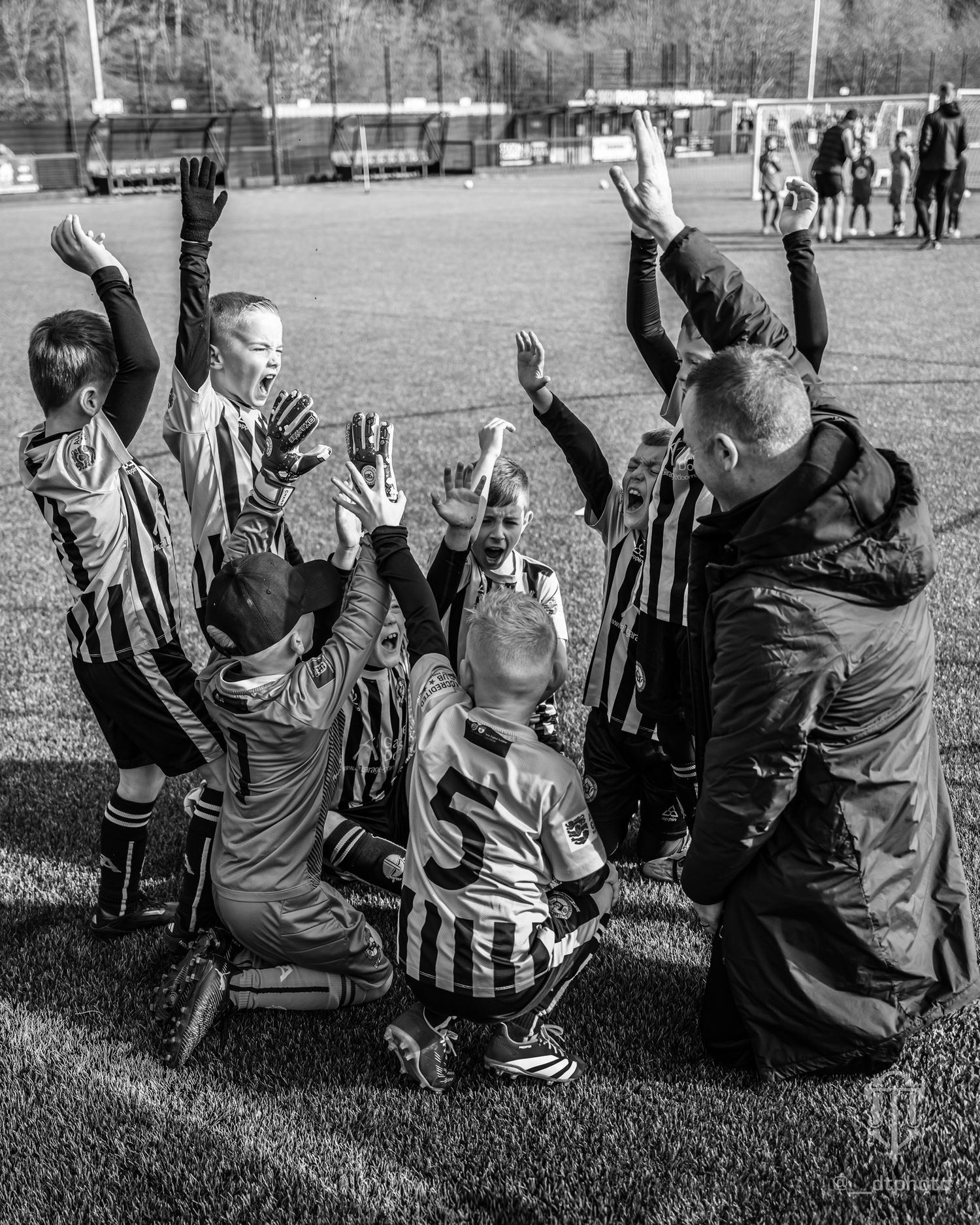 Black and white photo of a happy soccer celebration with players and coaches raising hands on a sports field.