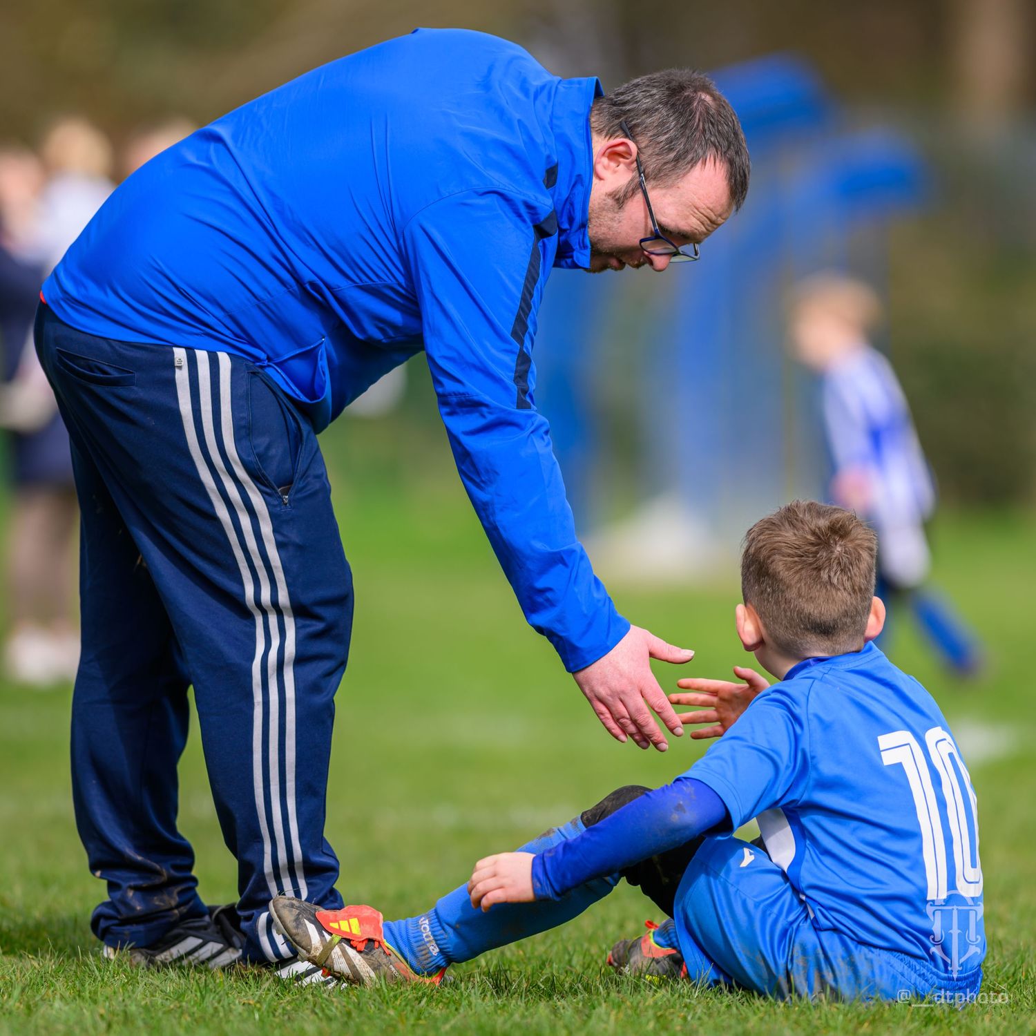 Coach provides encouragement to a young player in blue uniform during a football match.
