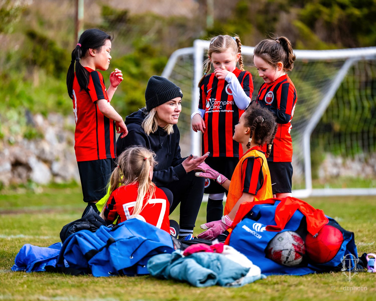 Football coach provides guidance to young players sitting on equipment bags during break.