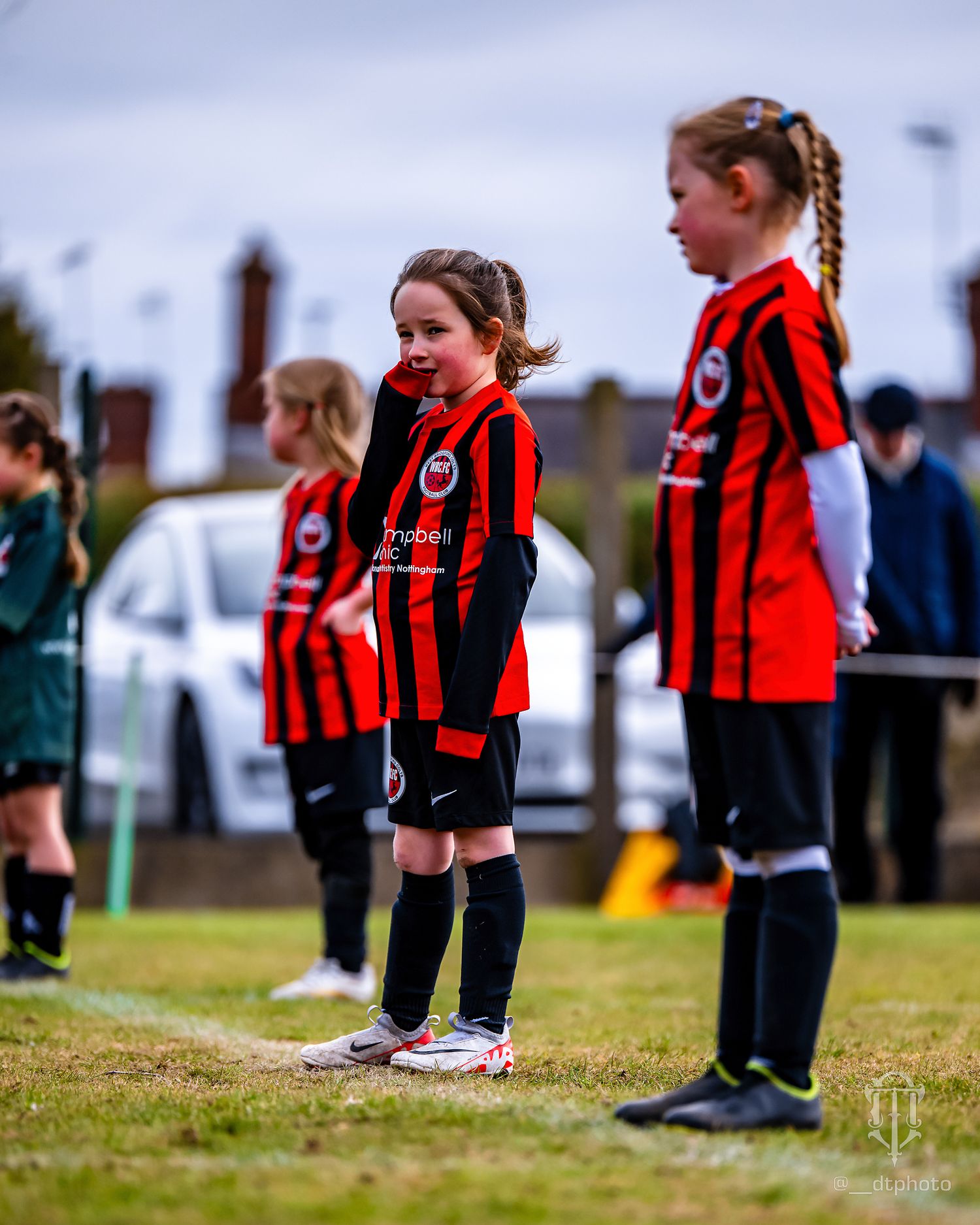 Young soccer players in red and black striped uniforms stand on a grass field during a match.