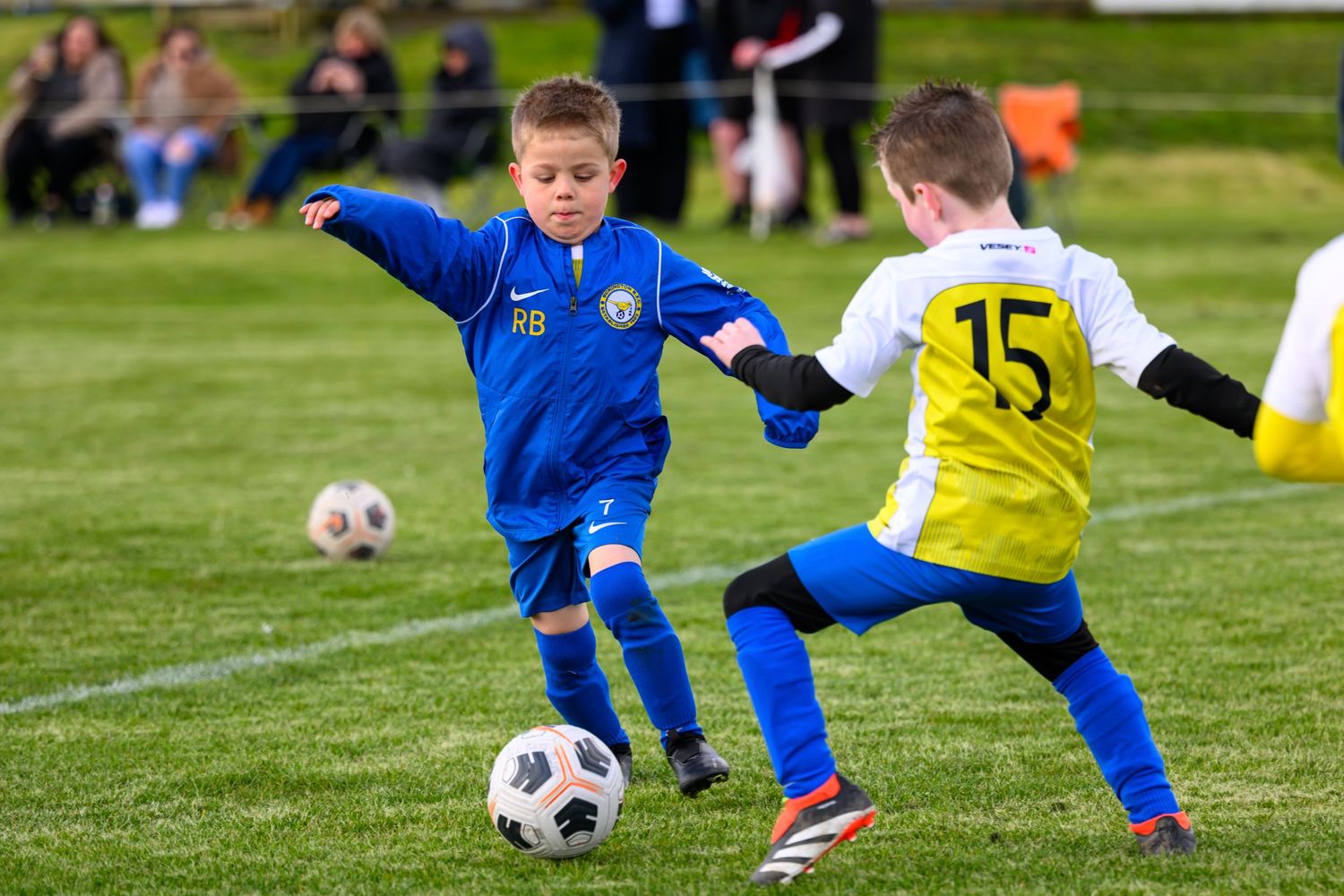 Two young soccer players compete for the ball during a youth match on a grass field.