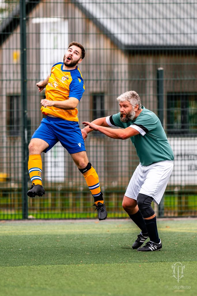 Two football players competing for the ball on an artificial turf field with one player jumping in the air.