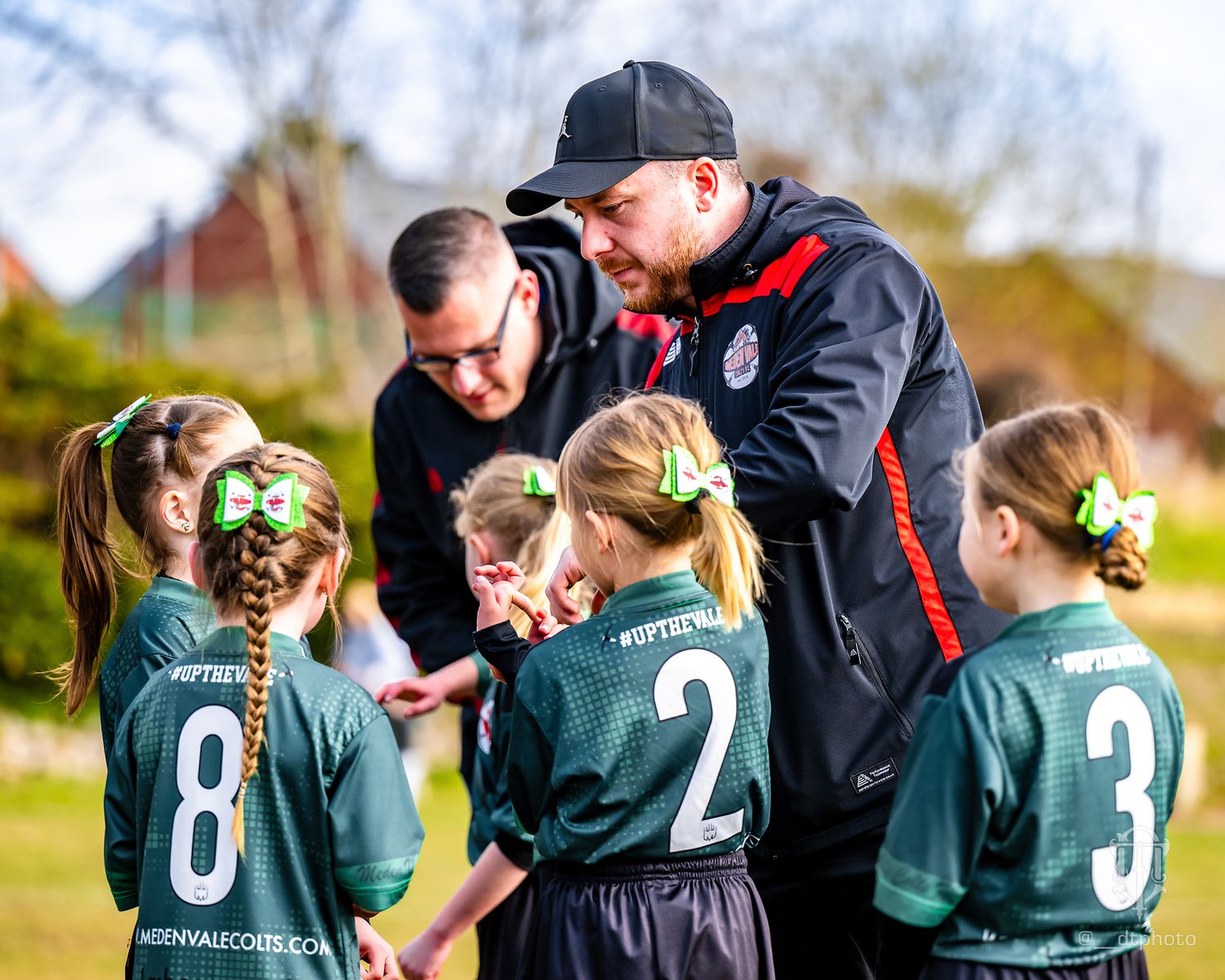 Coaches give instructions to youth football players in green uniforms during a game.