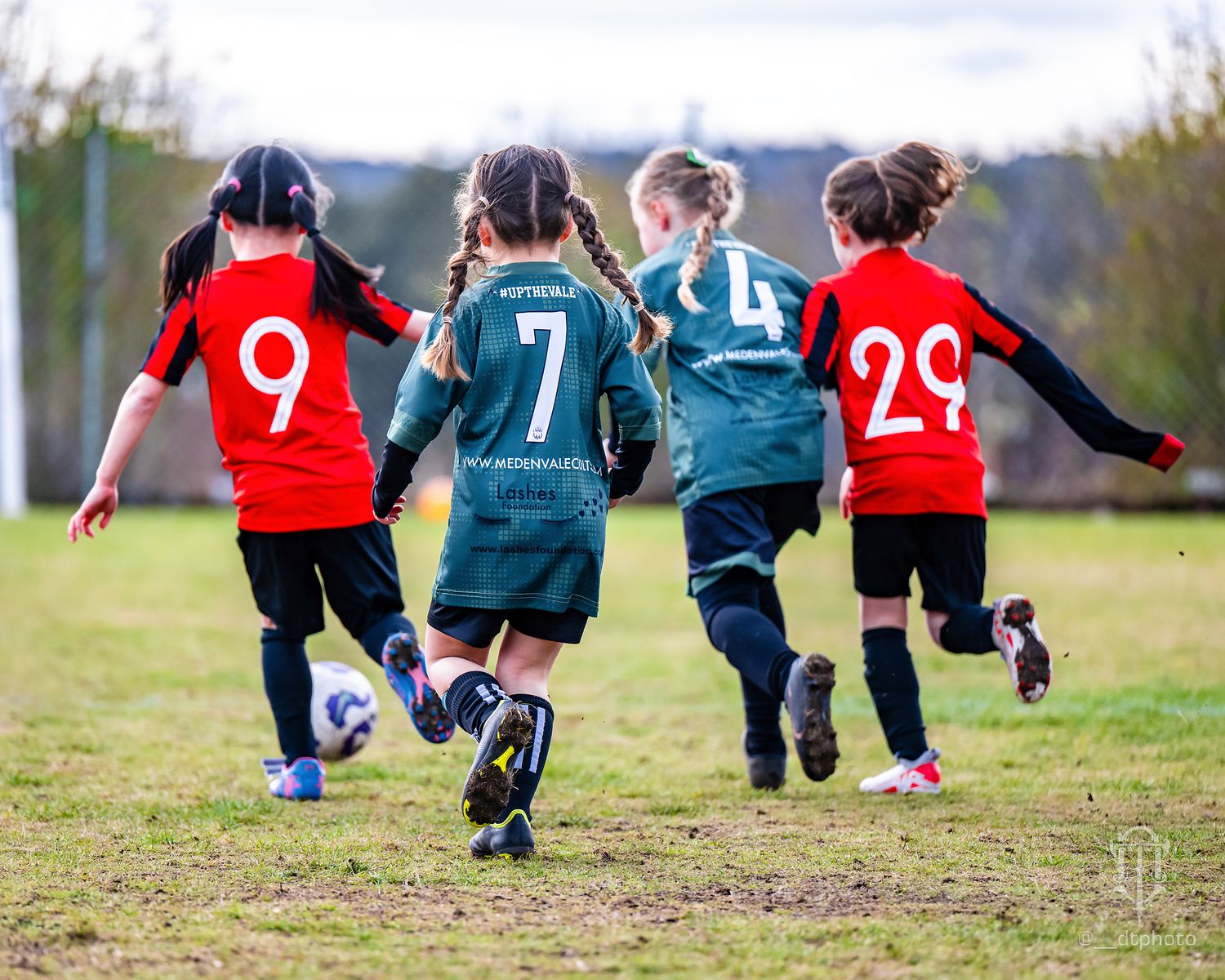 Four youth footballplayers running together on field wearing red and blue jerseys.