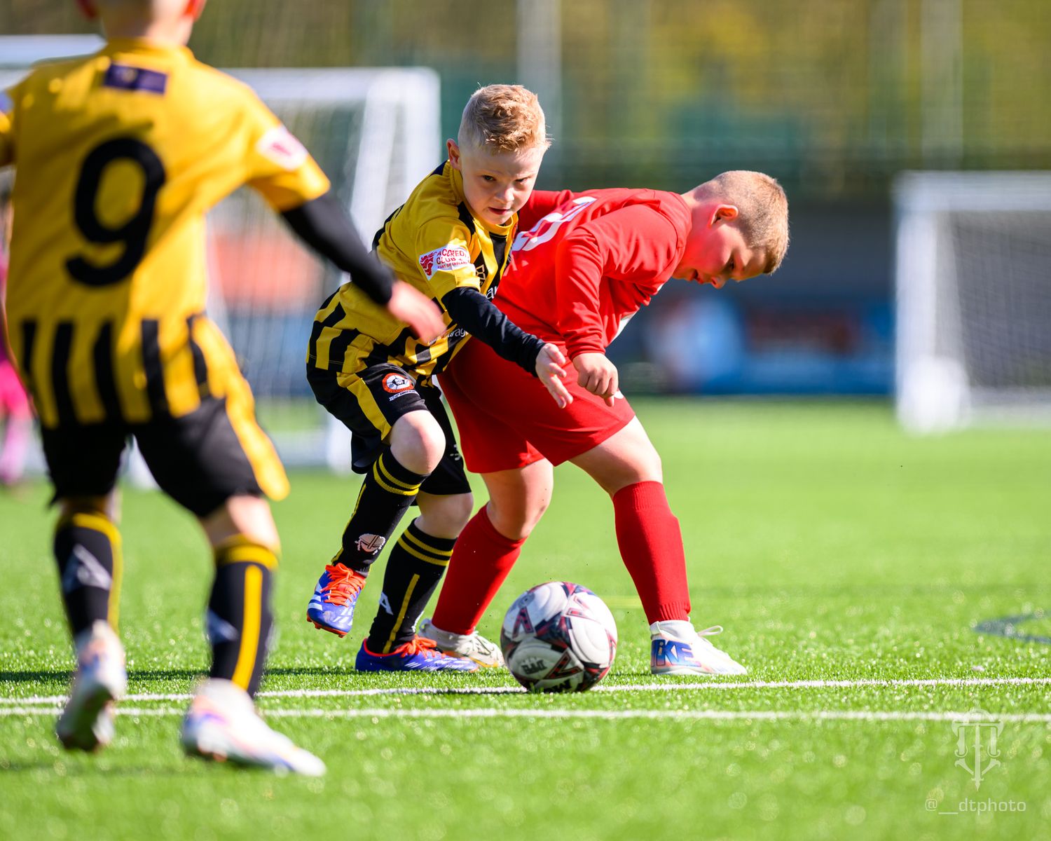 Soccer players in red and yellow jerseys battle for control of the ball during an intense match.