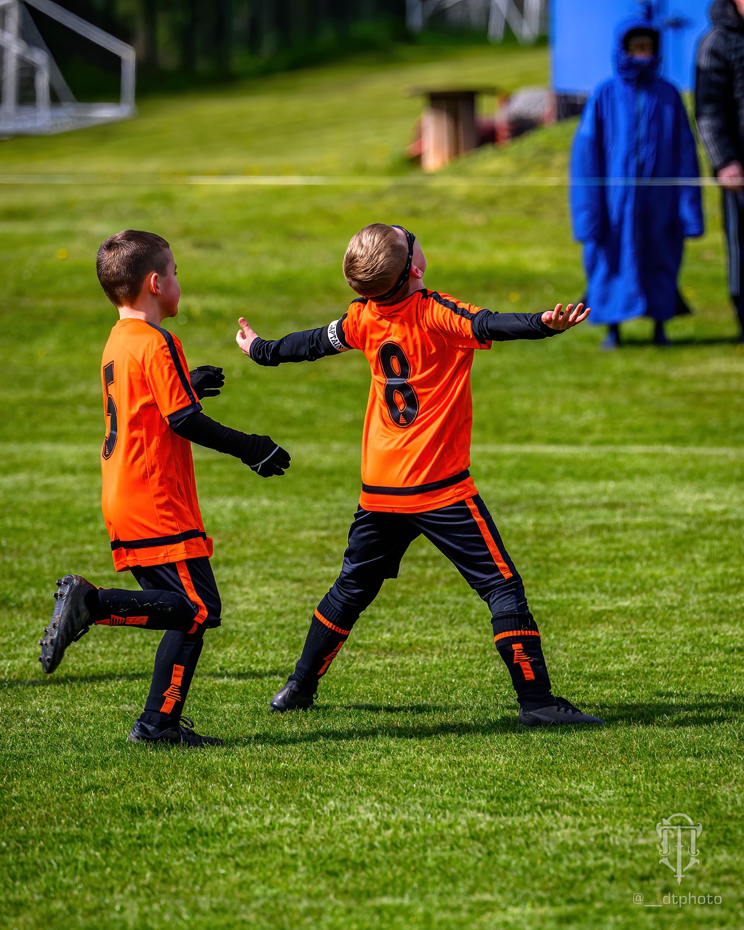 Two young players in orange football shirts celebrating a football goal.