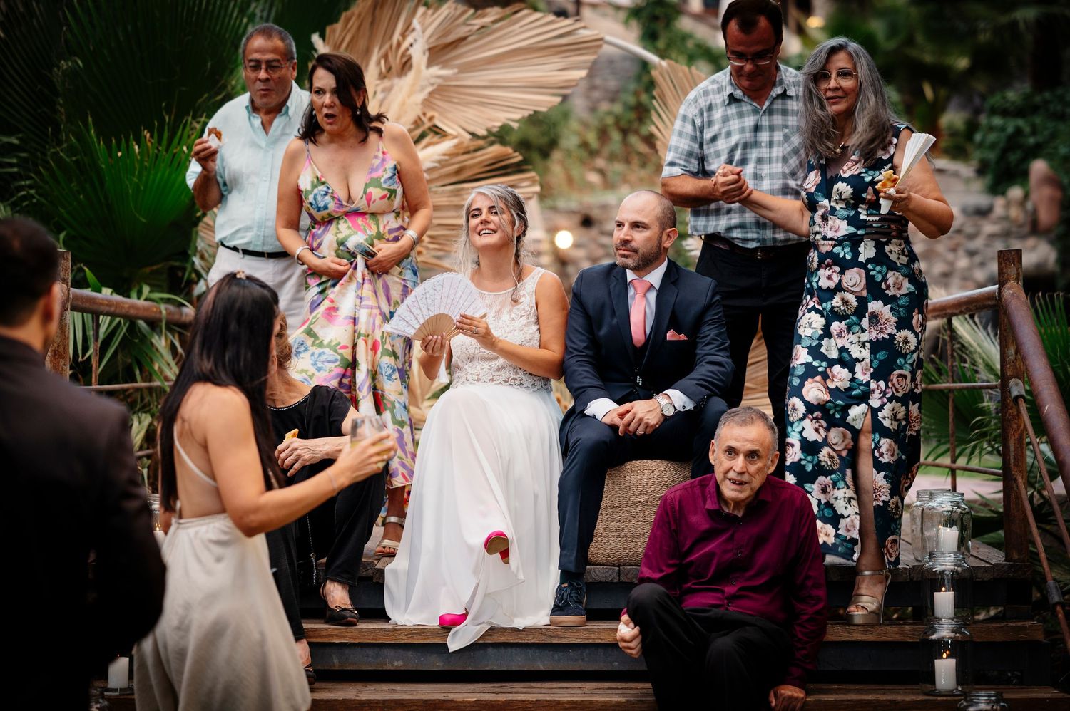 Guests celebrating at an outdoor wedding ceremony as confetti floats through the air on wooden deck steps.