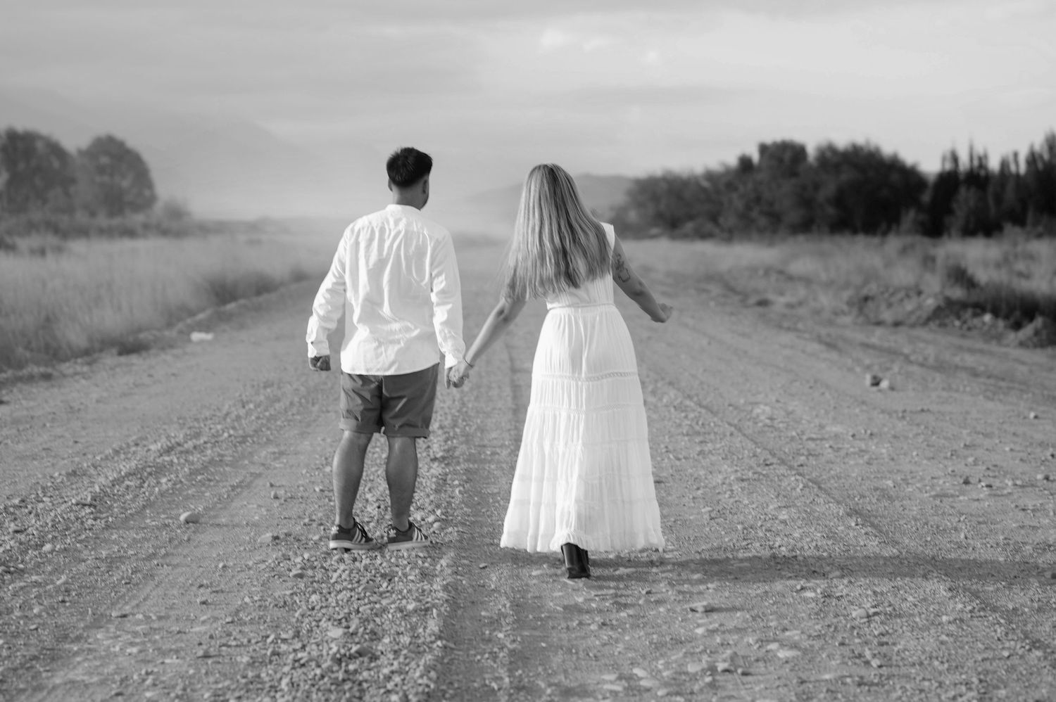 A couple walking hand in hand down a rural dirt road in black and white photography.