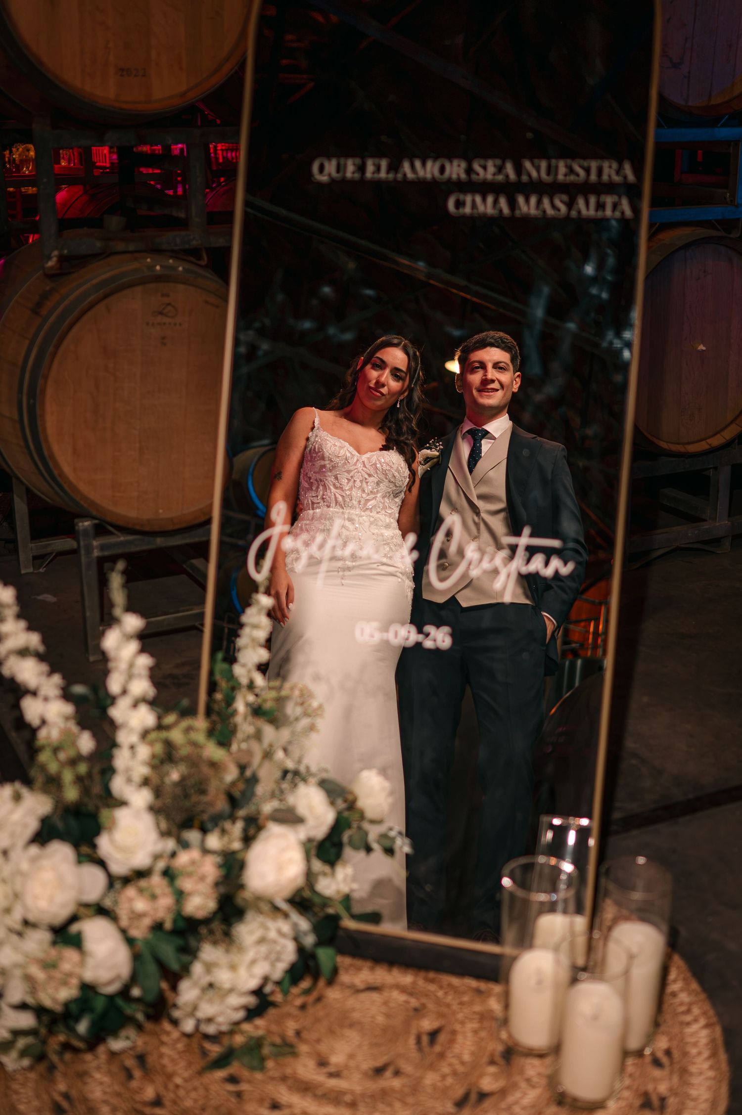 Bride and groom posing in front of a gold mirror at a winery wedding with white floral arrangements and candles.